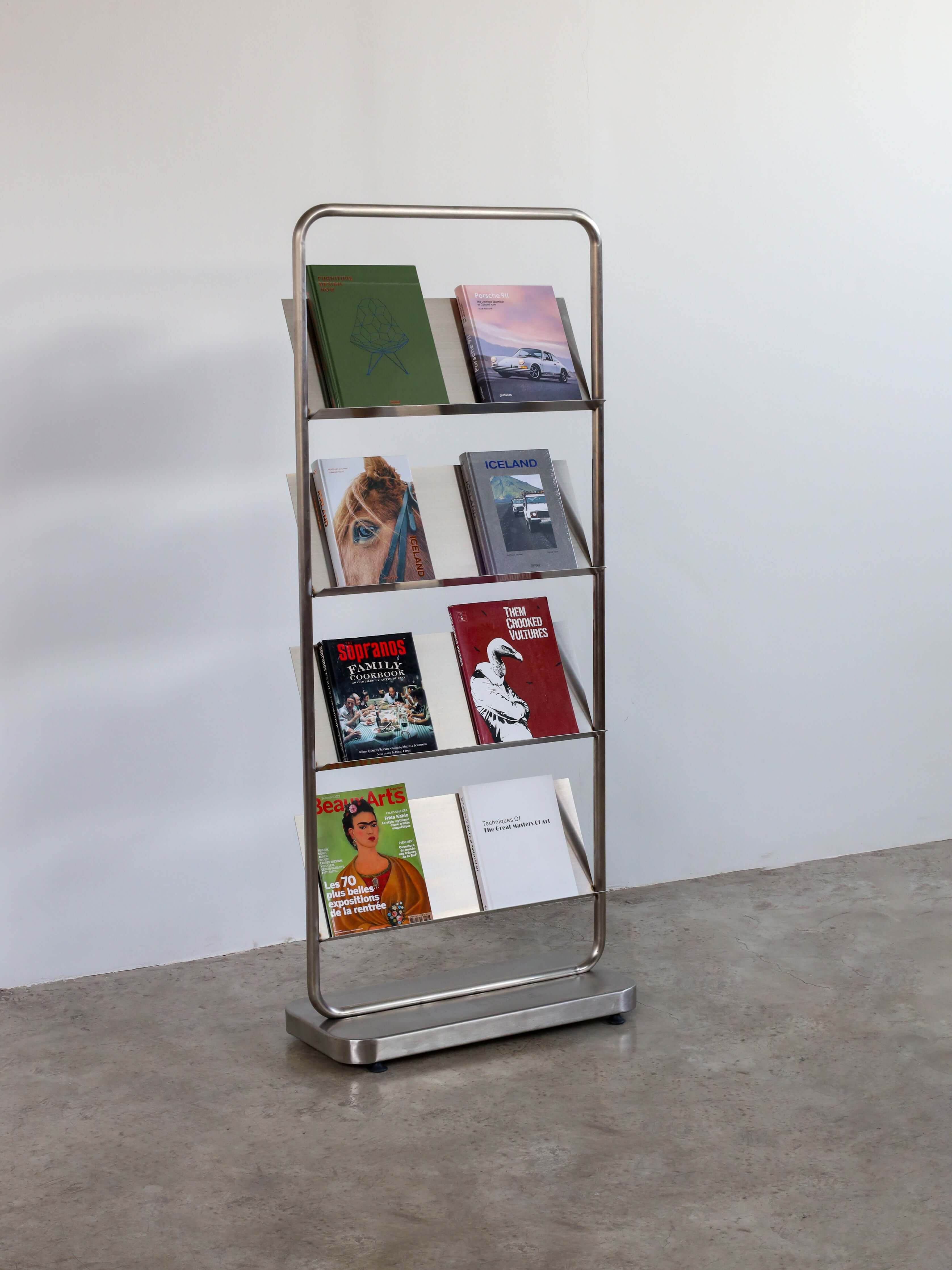 Stainless steel bookshelf with books against a white wall