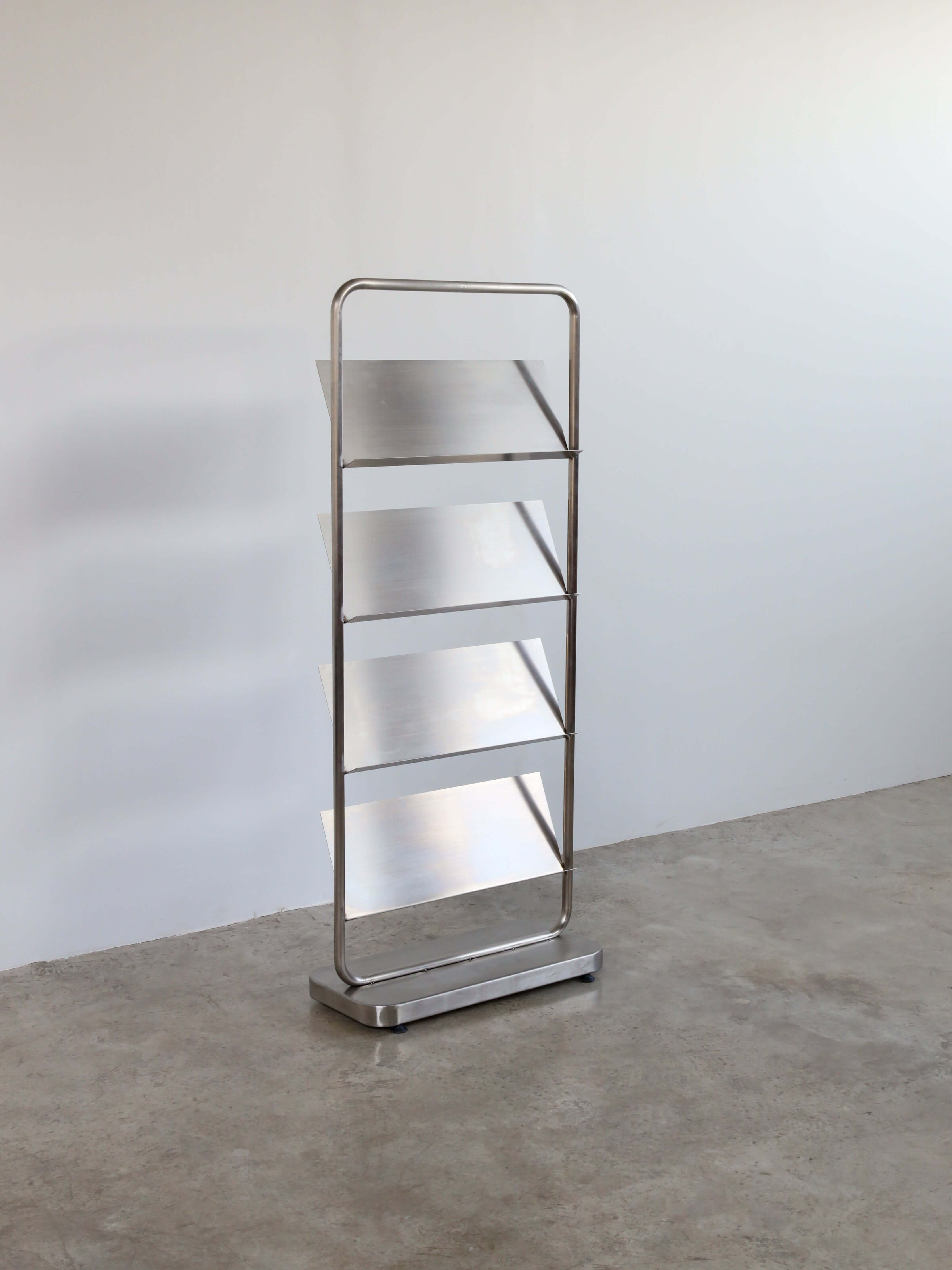 Stainless steel bookshelf with four shelves against a white wall.