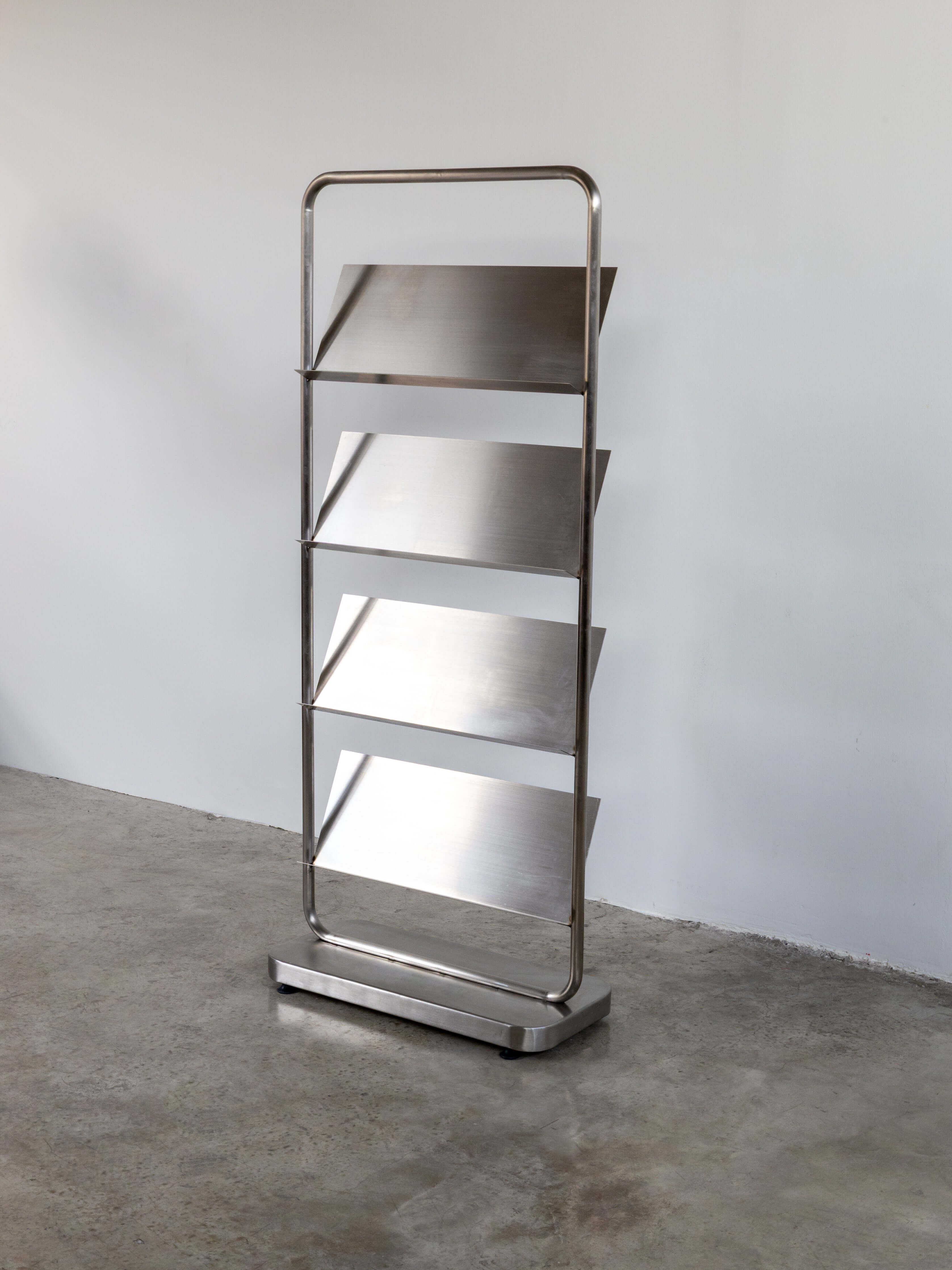 Stainless steel bookshelf with four shelves against a plain wall.