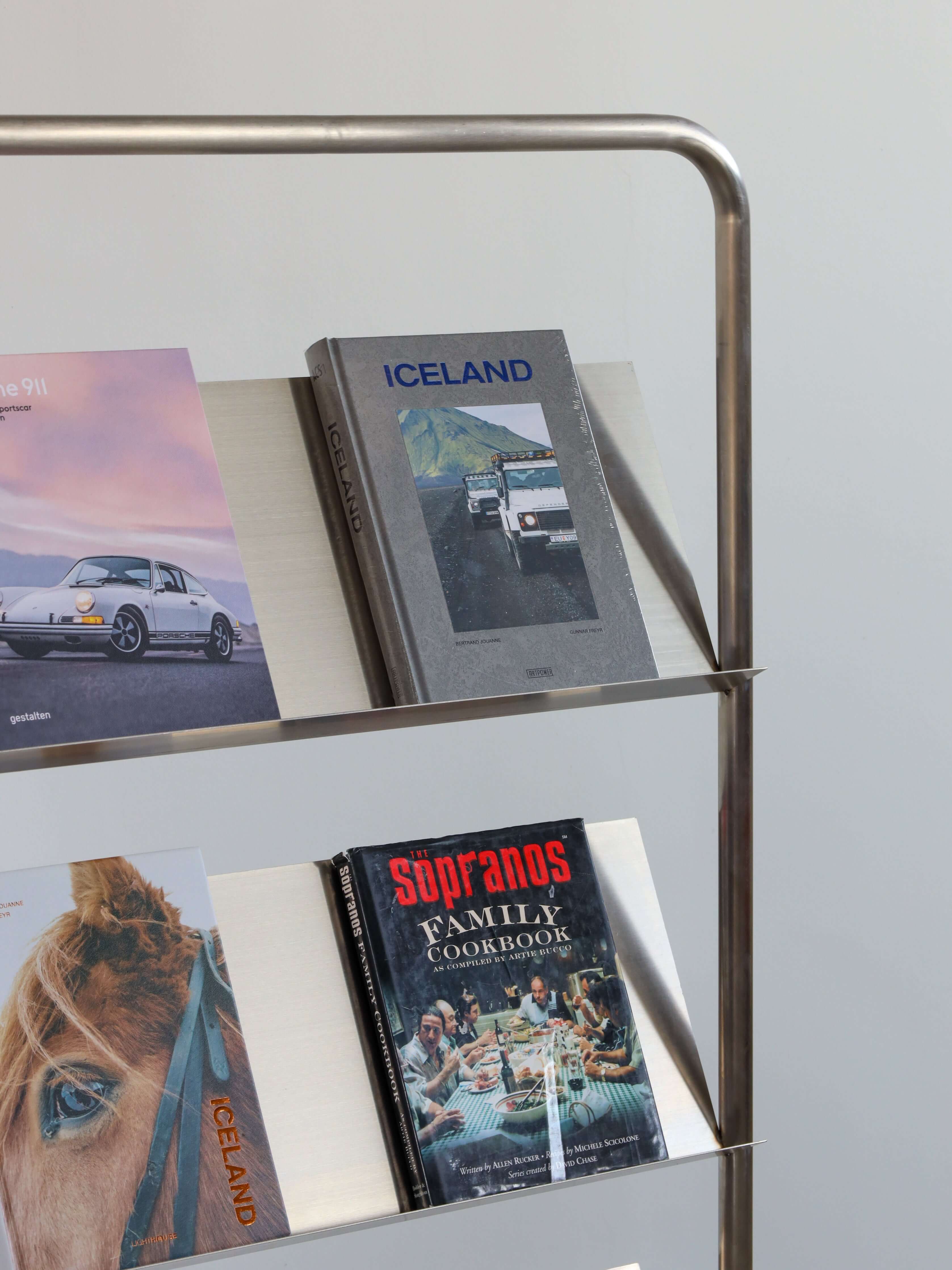 Stainless steel bookshelf with books titled 'Iceland' and 'Sourdos Family Cookbook' against a light gray background.
