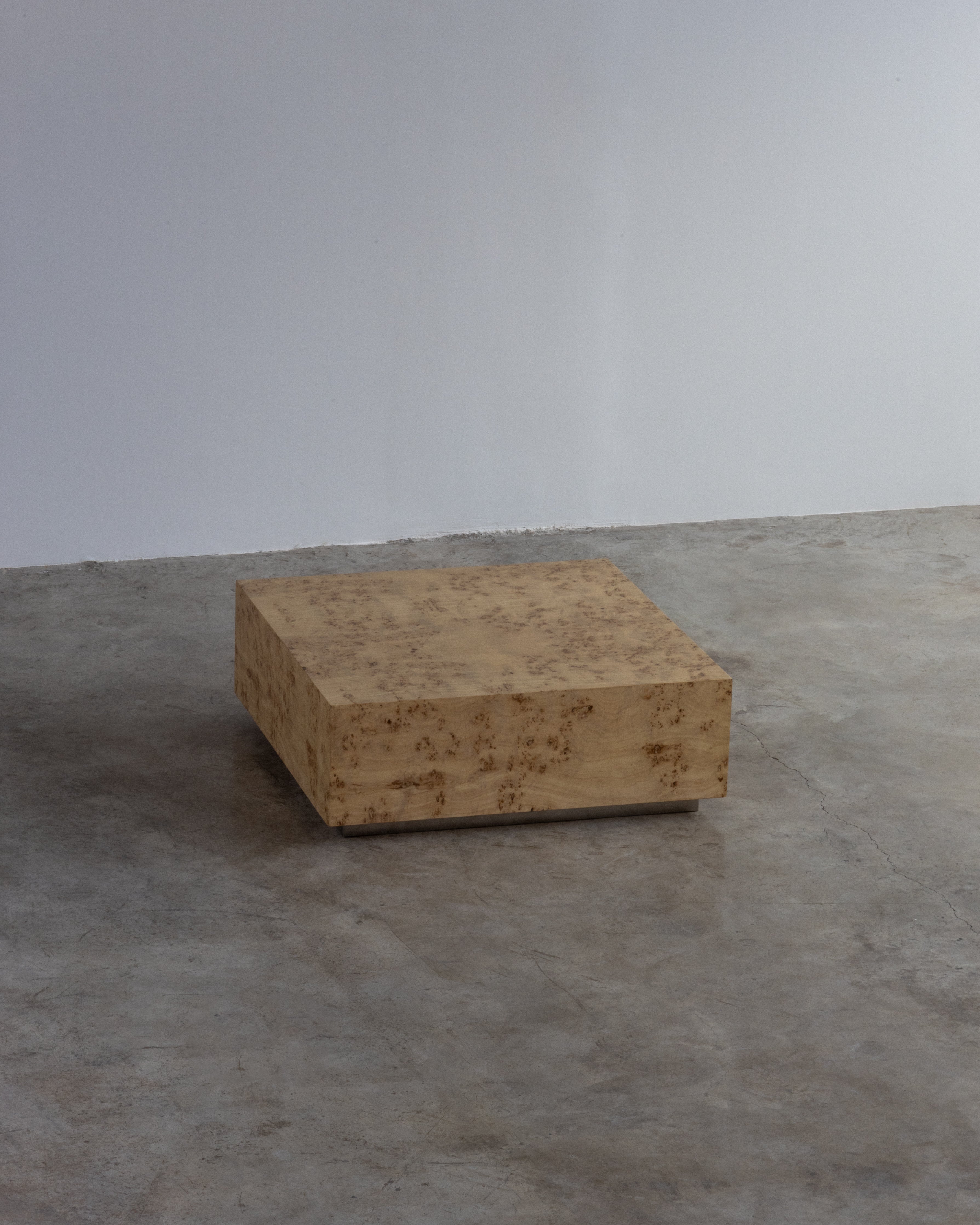 A burlwood vintage coffee table with a square shape and a visible grain pattern, placed on a concrete surface.