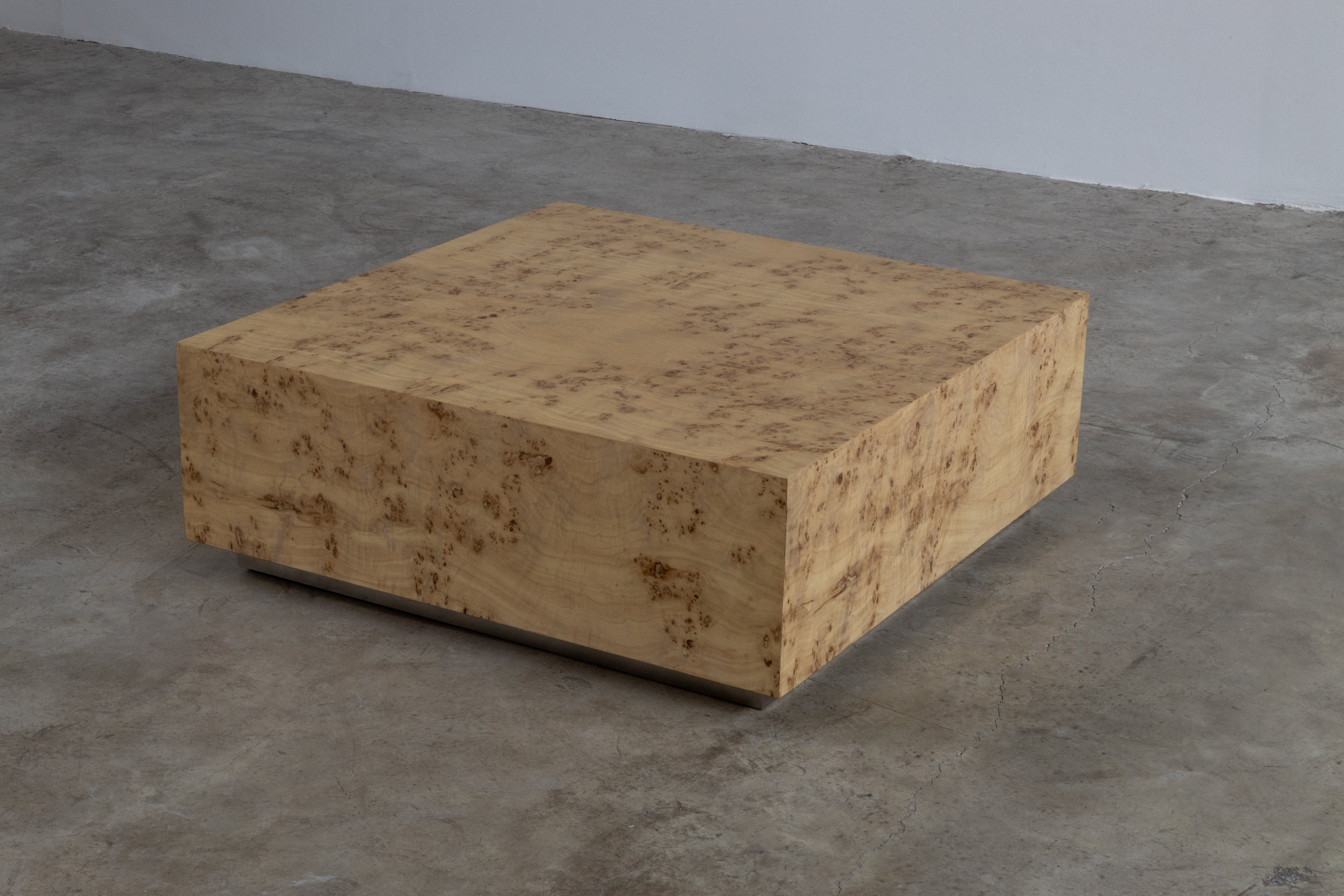 A rectangular brown burlwood coffee table on a grey floor against a white wall.