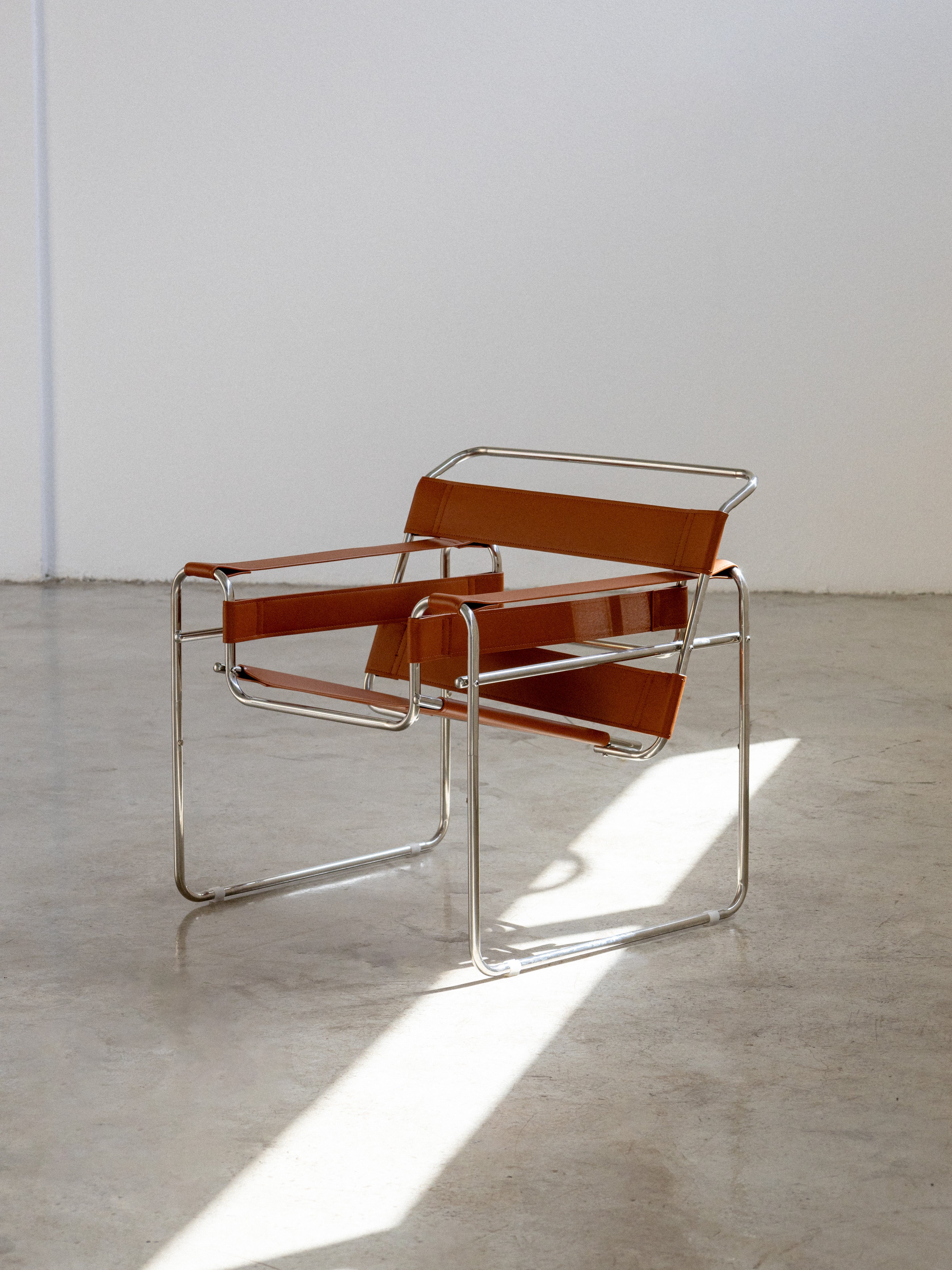 A Wassily chair with chrome frame and brown leather seating surface, placed in a room with natural lighting.