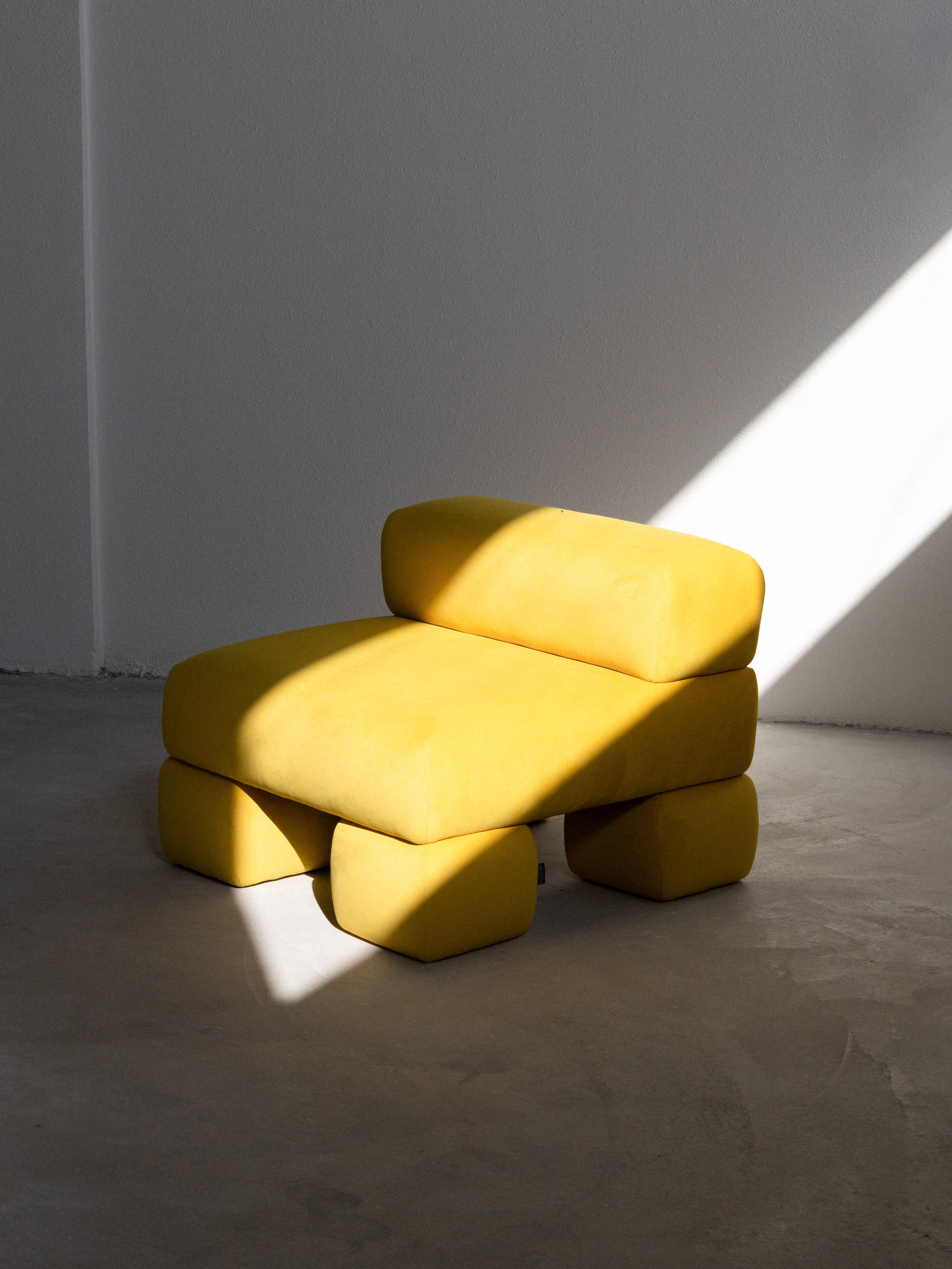 A bright yellow upholstered sofa with a unique, minimalist design, featuring a low back and a modern aesthetic.