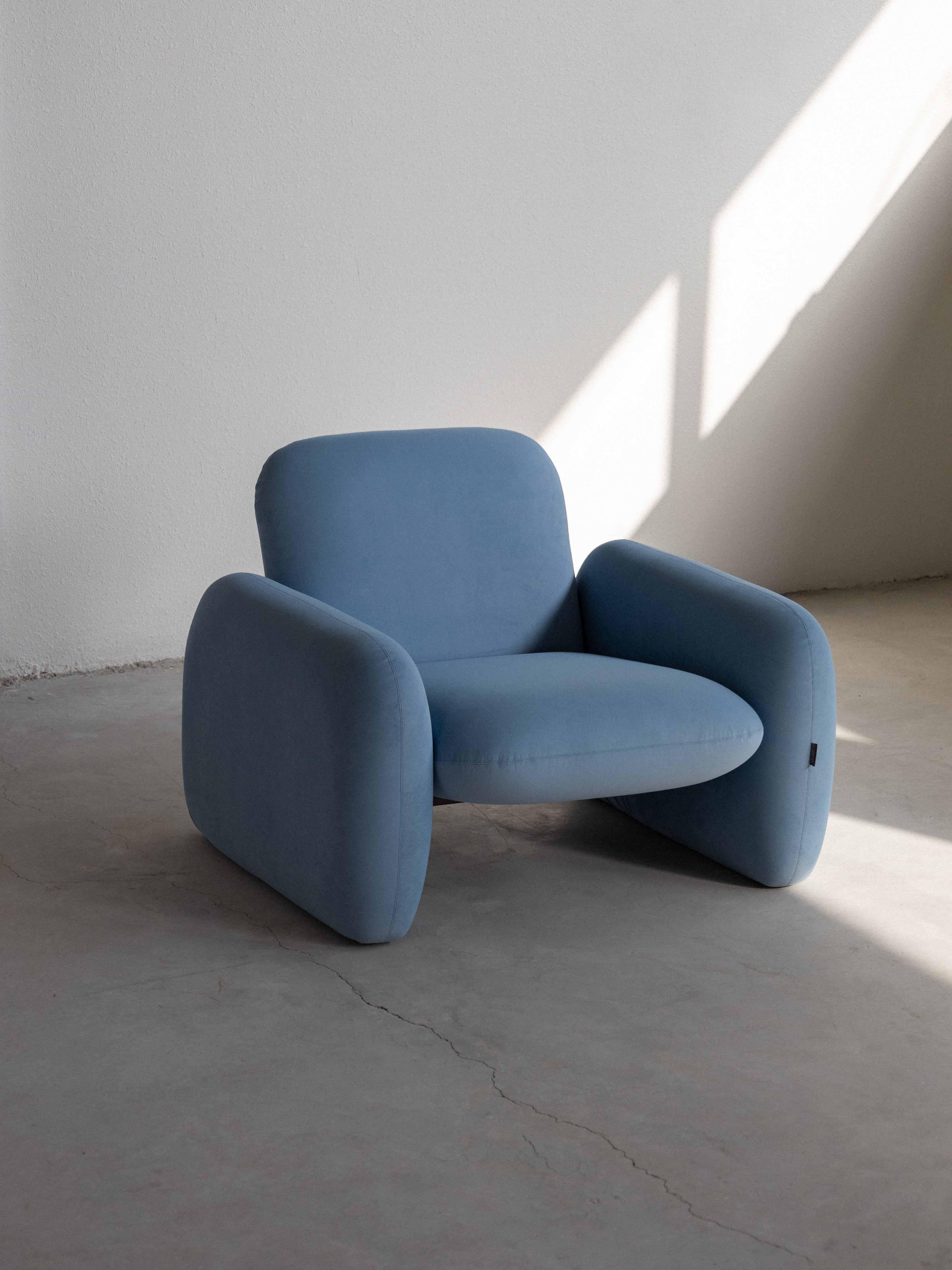 A blue upholstered armchair with a minimalist design, featuring a smooth solid color without any patterns.