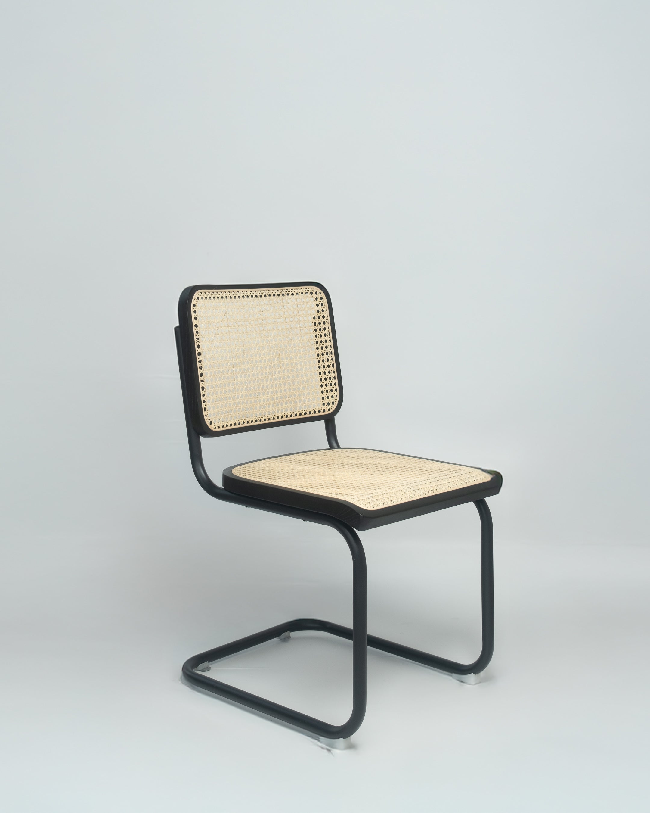 A black Cesca chair with a rattan seat and backrest, positioned against a neutral background.