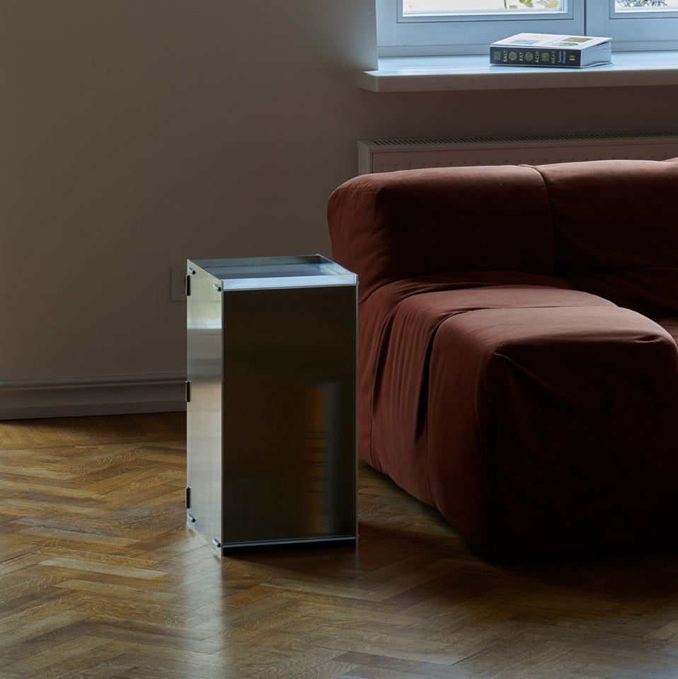 Modern metallic side table next to a brown sofa in a room with a window.