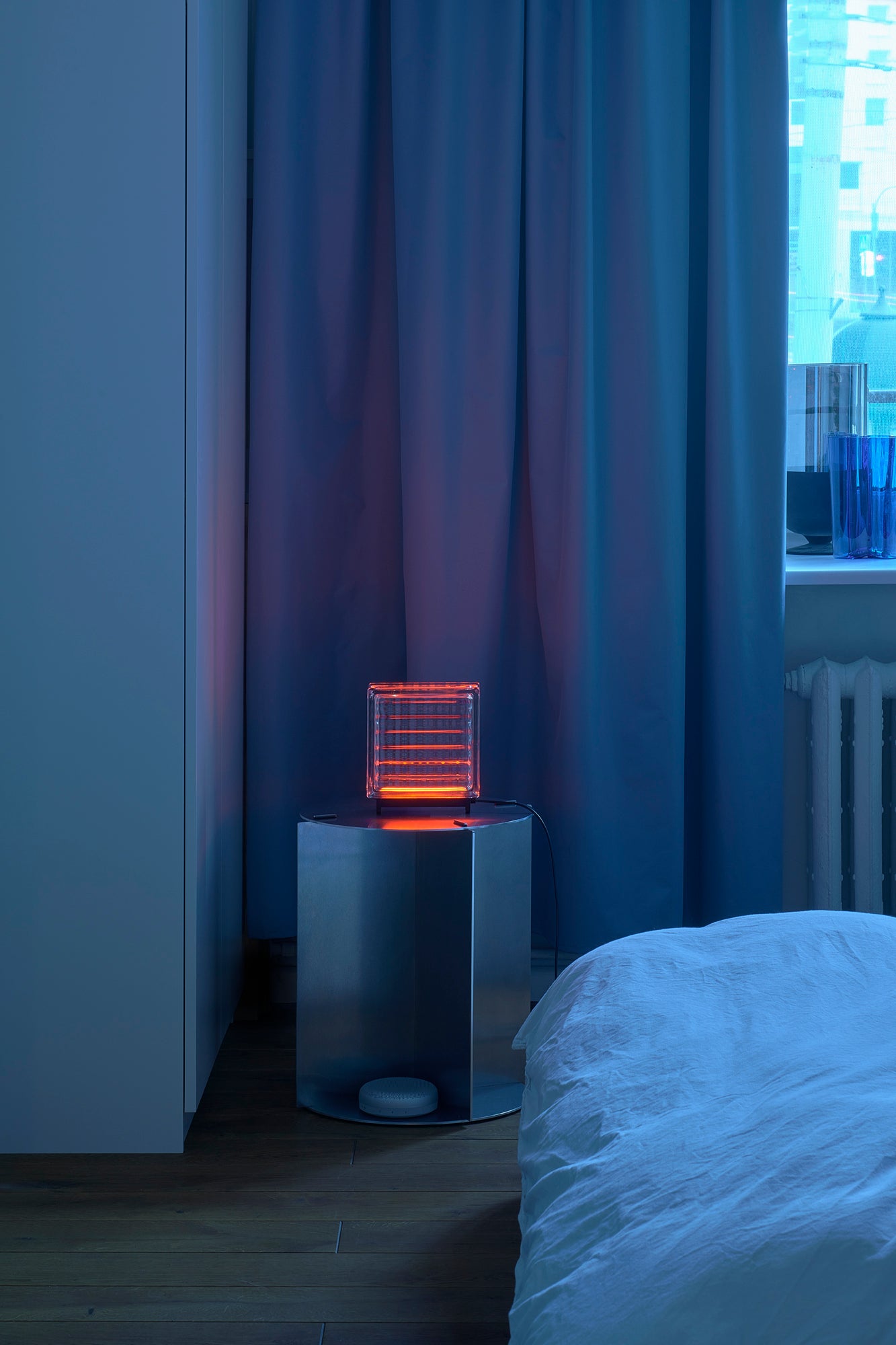 Neon orange light on a small table next to a bed with curtains in the background