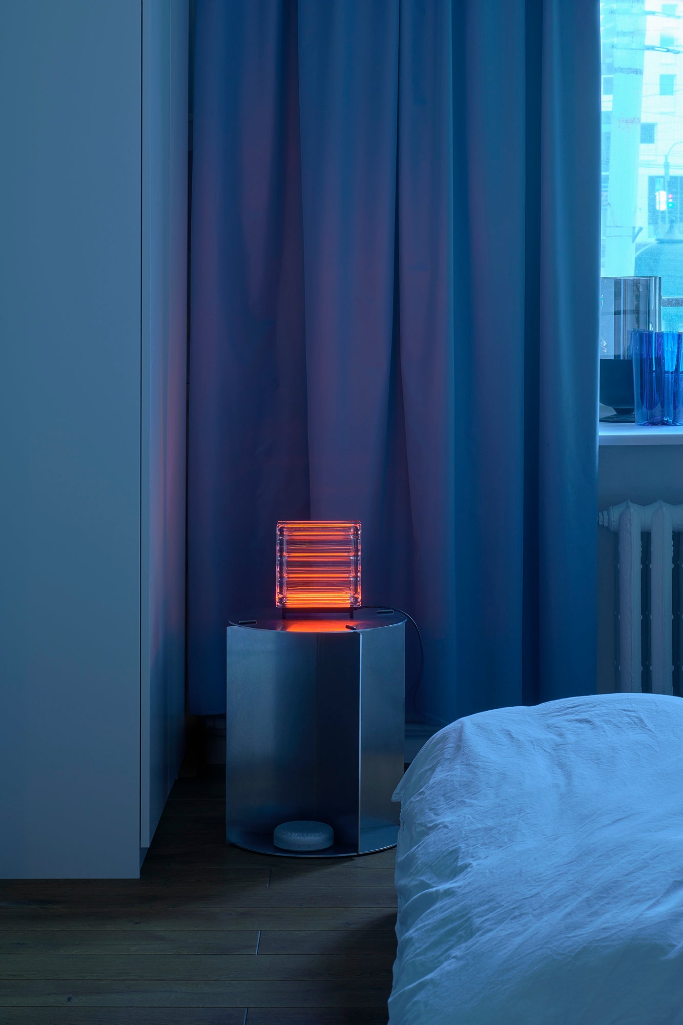 Neon light on a small table in a bedroom with blue curtains and a bed.