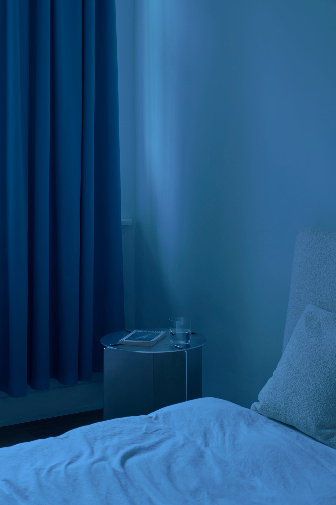 Bedroom with blue lighting, bed, nightstand, and curtain.