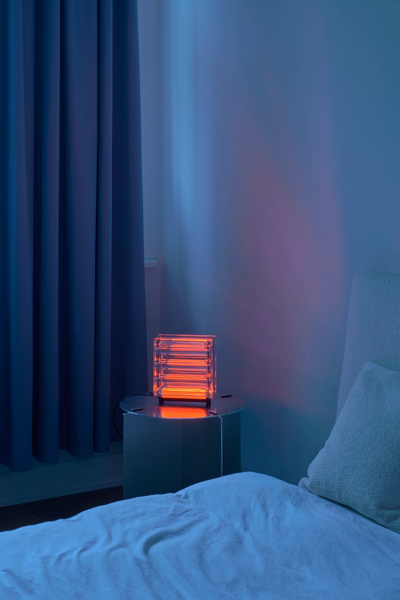 Neon orange light on a nightstand next to a bed with blue curtains.