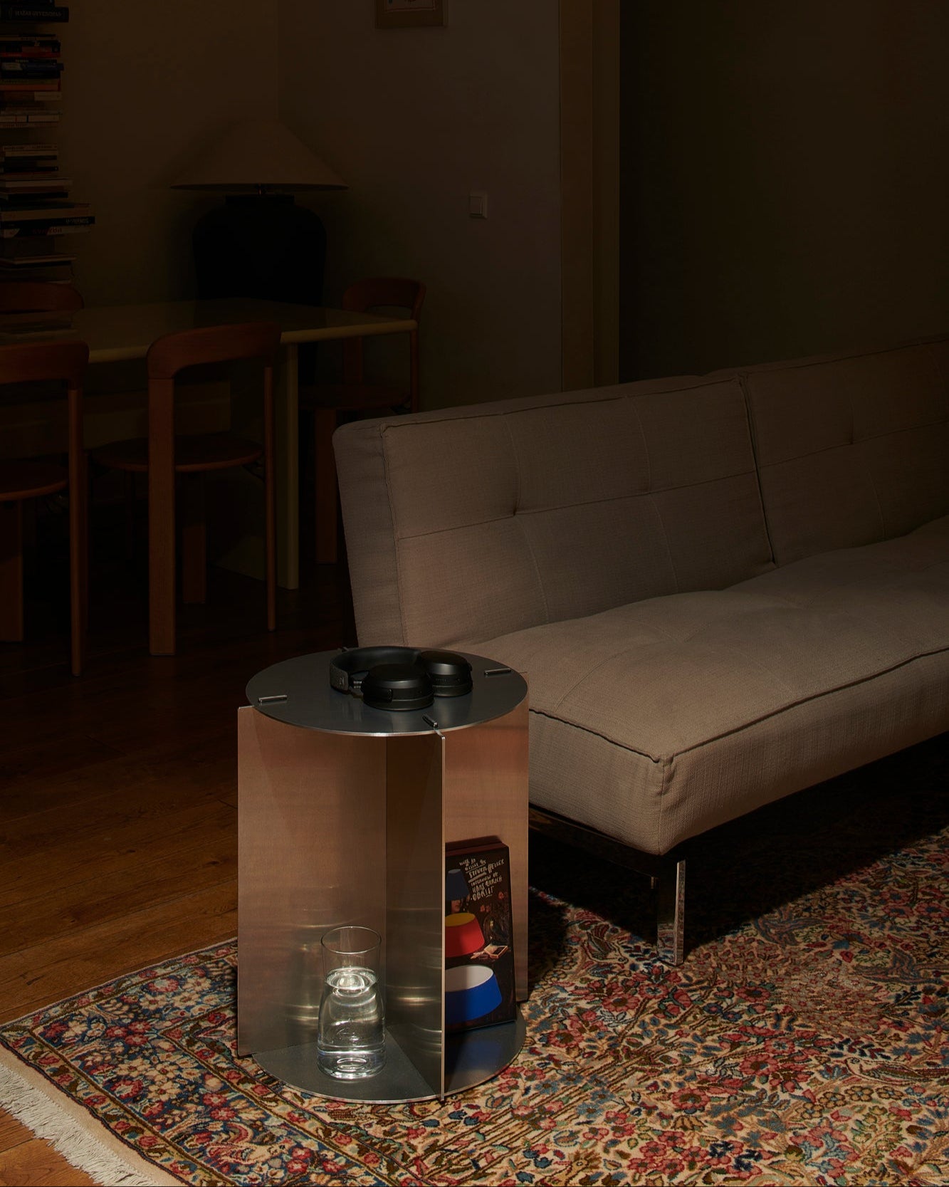 Small metallic table with a glass container on a patterned rug in a dimly lit room.