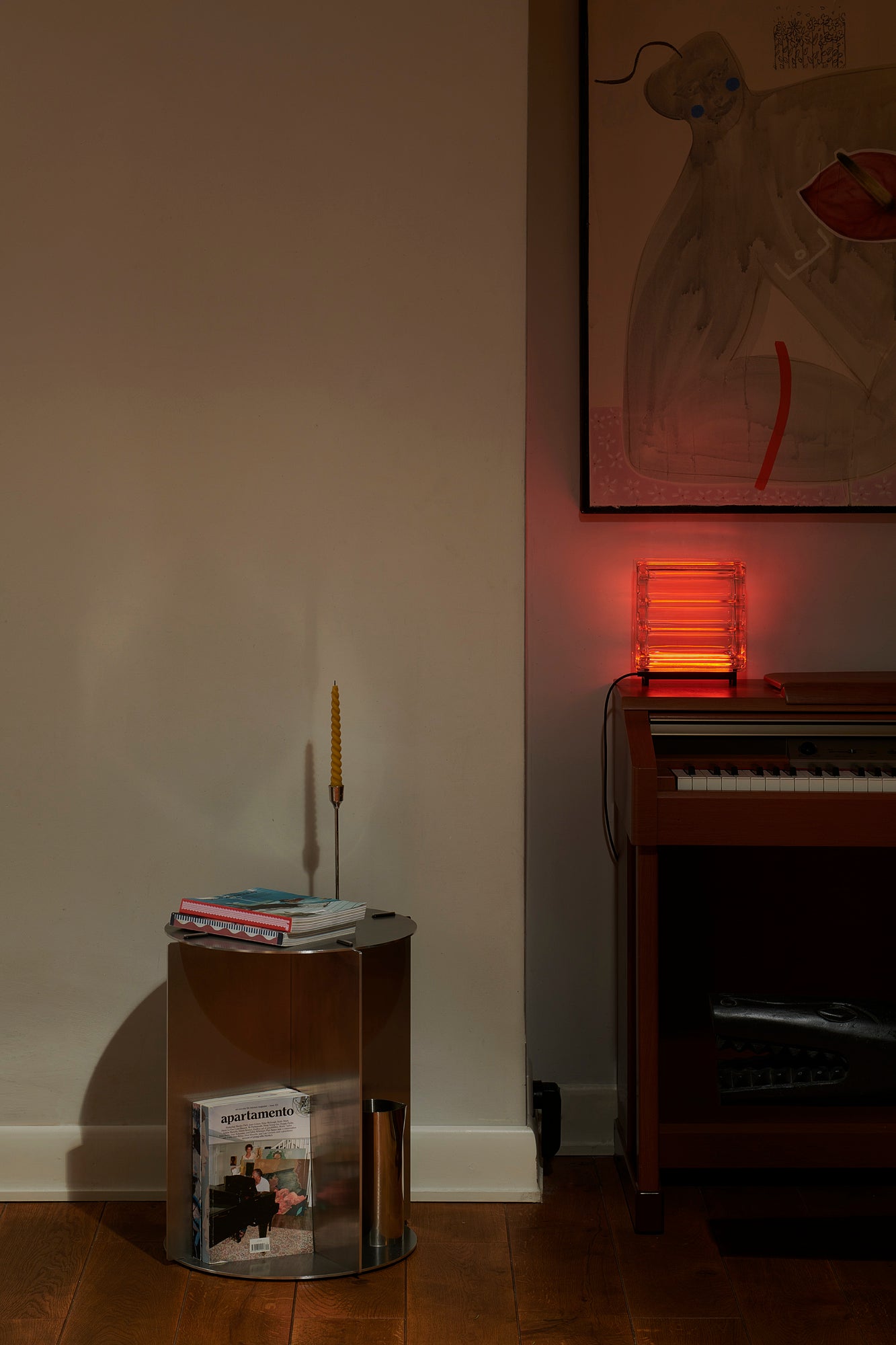 Small round table with books and a candle next to a piano in a dimly lit room.