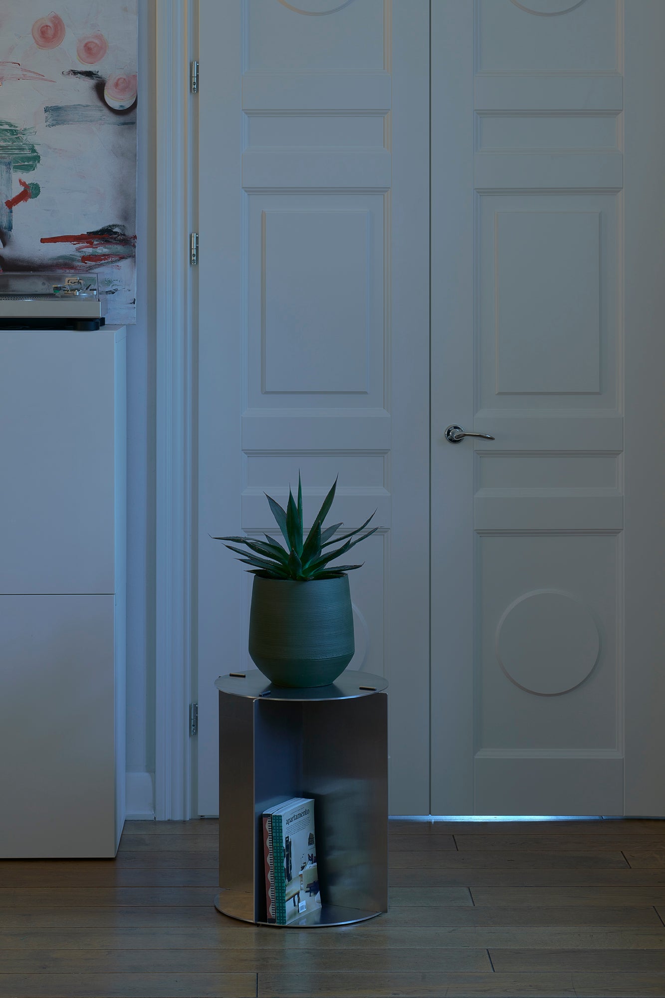 Small round table with a plant in front of a white door