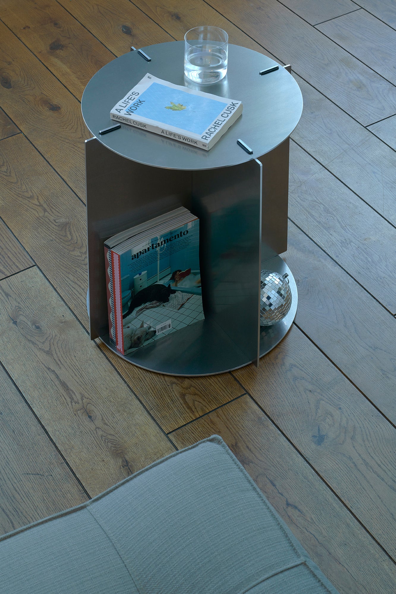 Small round metal table with books and a glass on a wooden floor