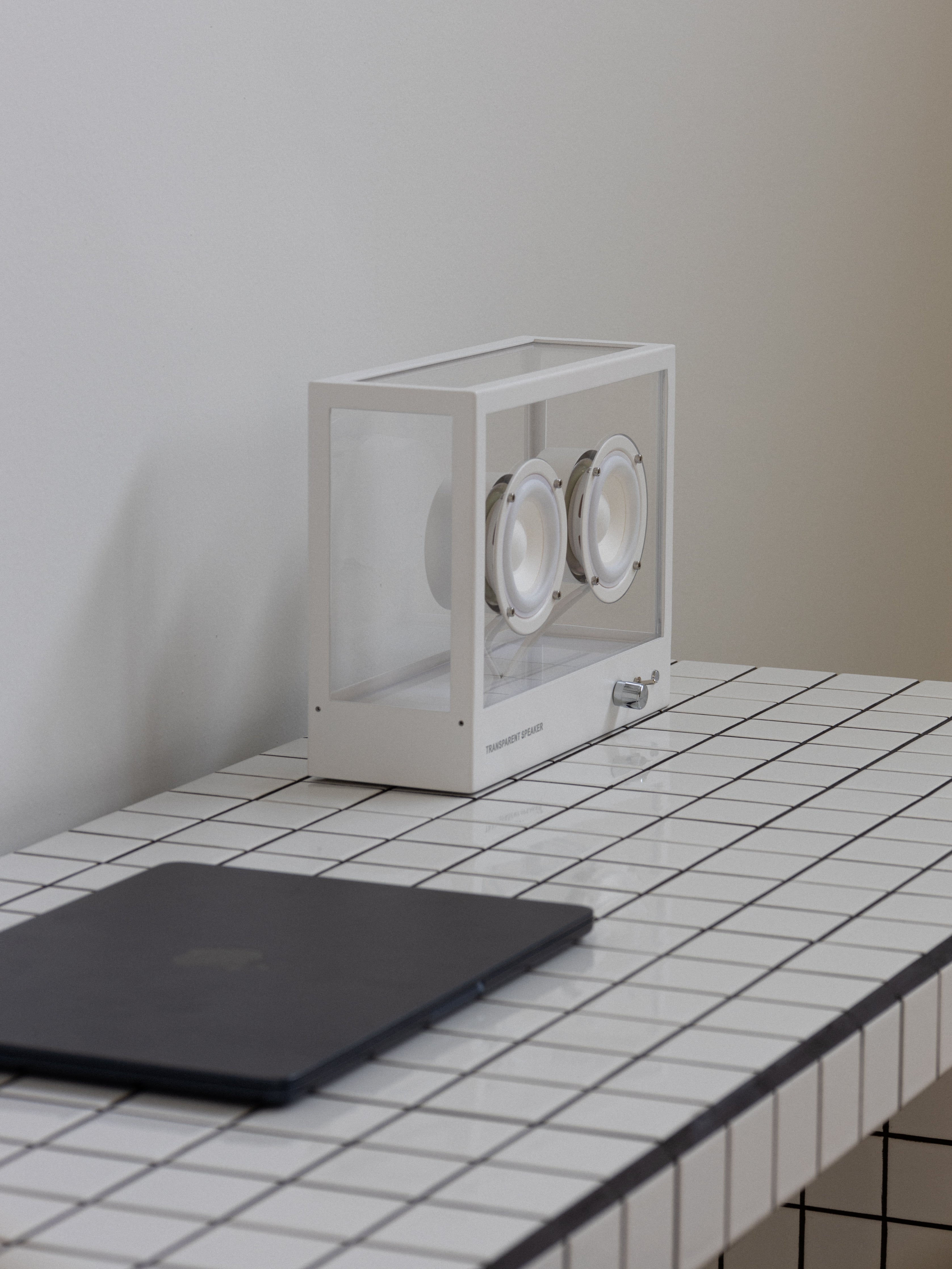 White rectangular watch winder on a tiled surface with a plain wall background