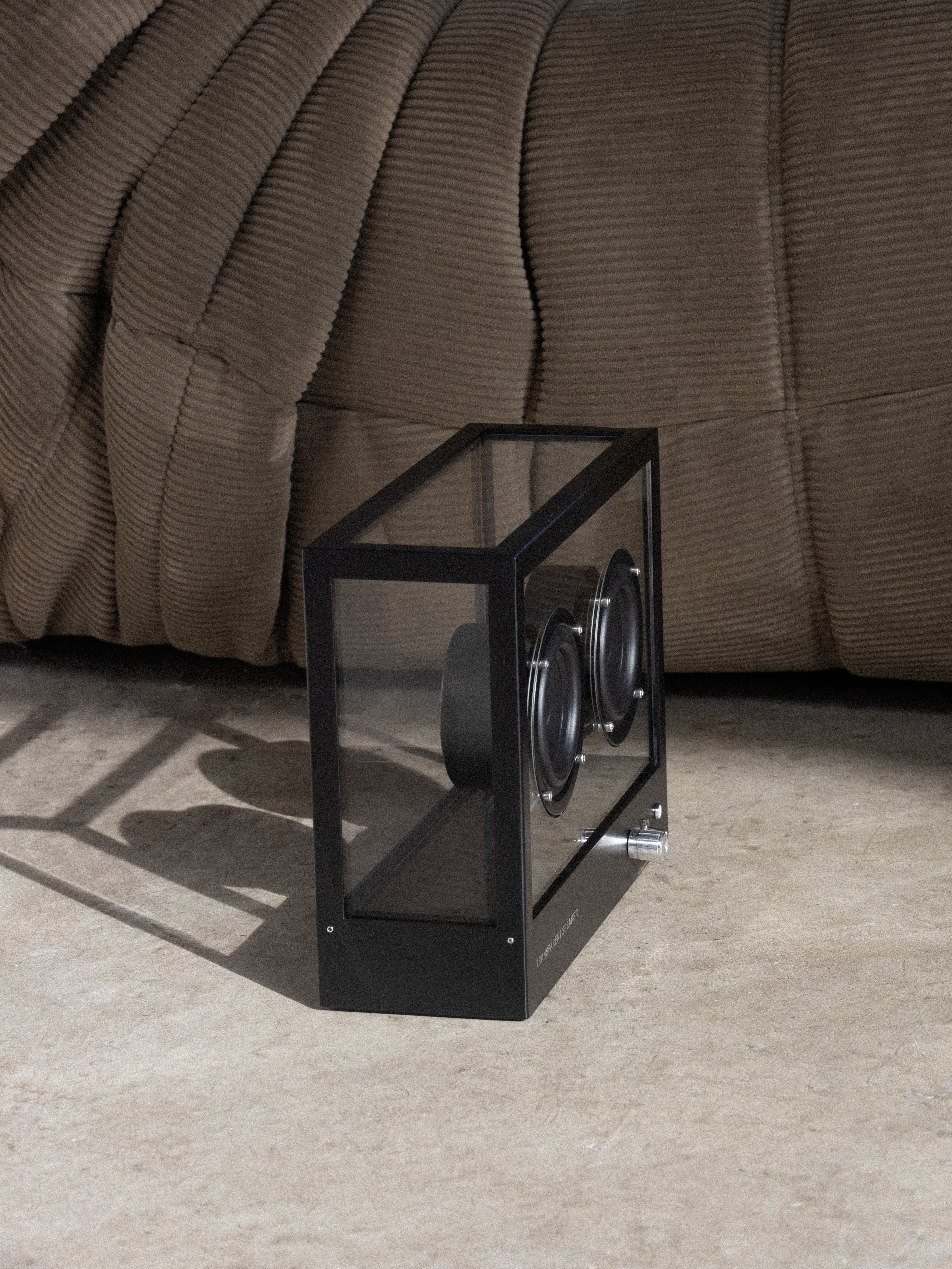 Black rectangular watch holder with two watches on a beige carpet next to a brown sofa.