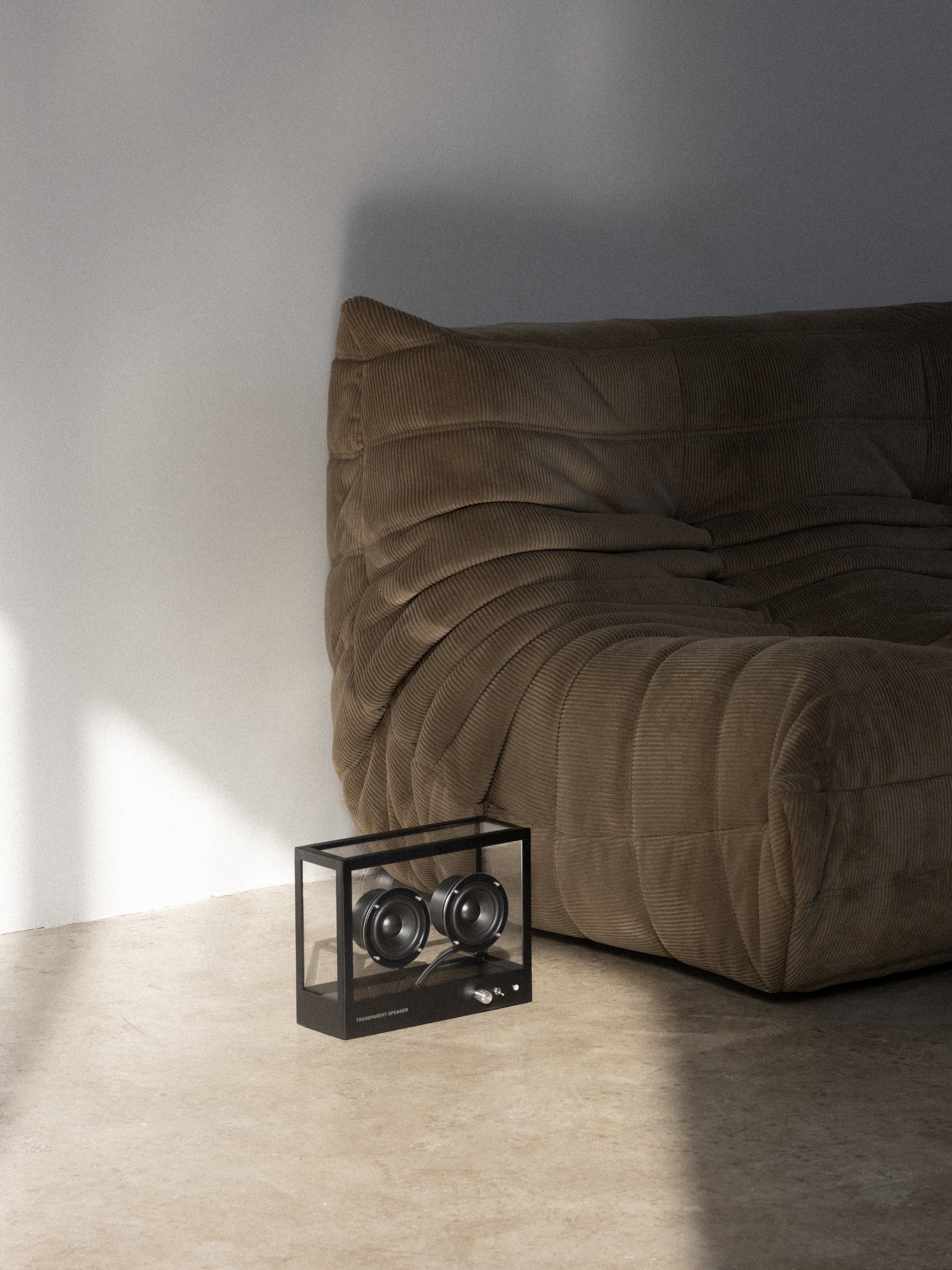 Brown sofa in a room with a small black table and speakers on a light gray floor.
