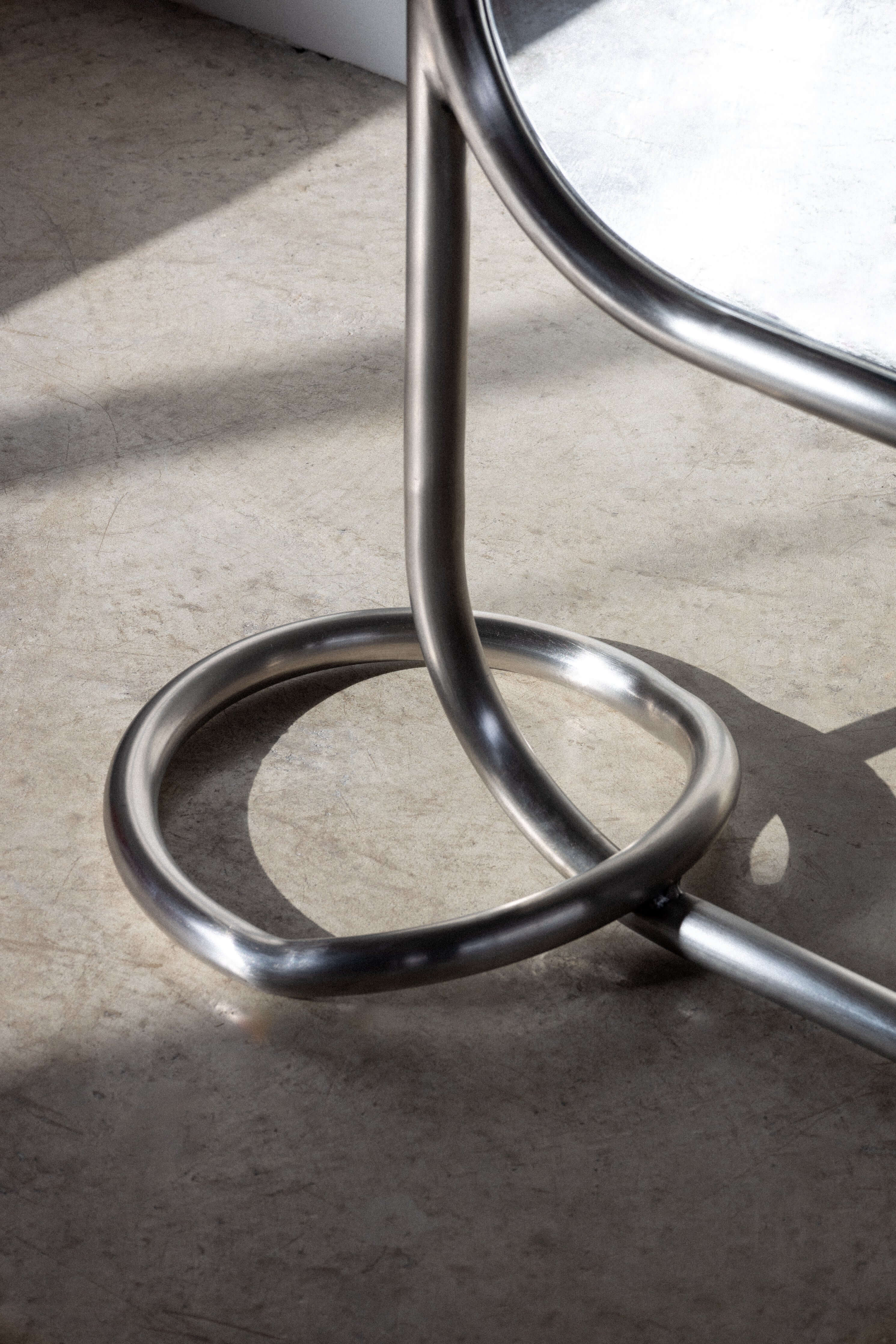 Freestanding stainless steel pipe mirror with brushed finish and circular base rings for stability.