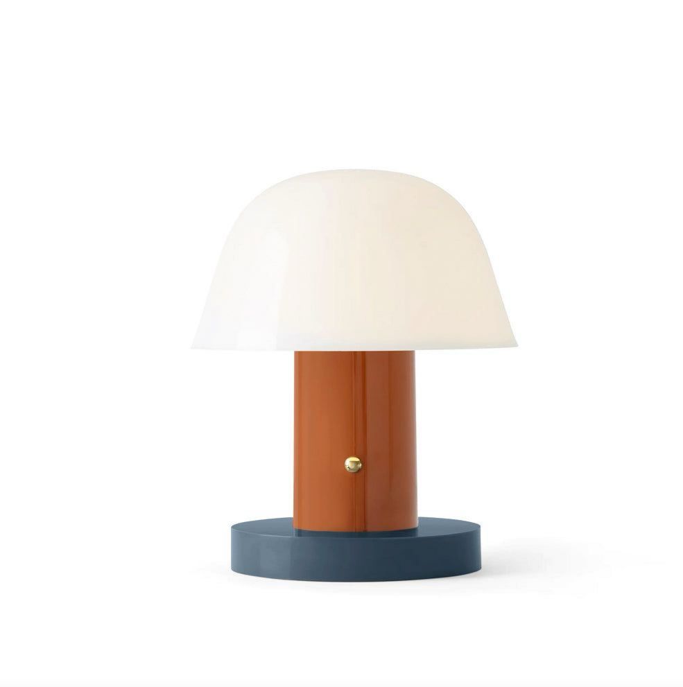A table lamp with a white shade, brown stem, and a black base, presented against a plain background.