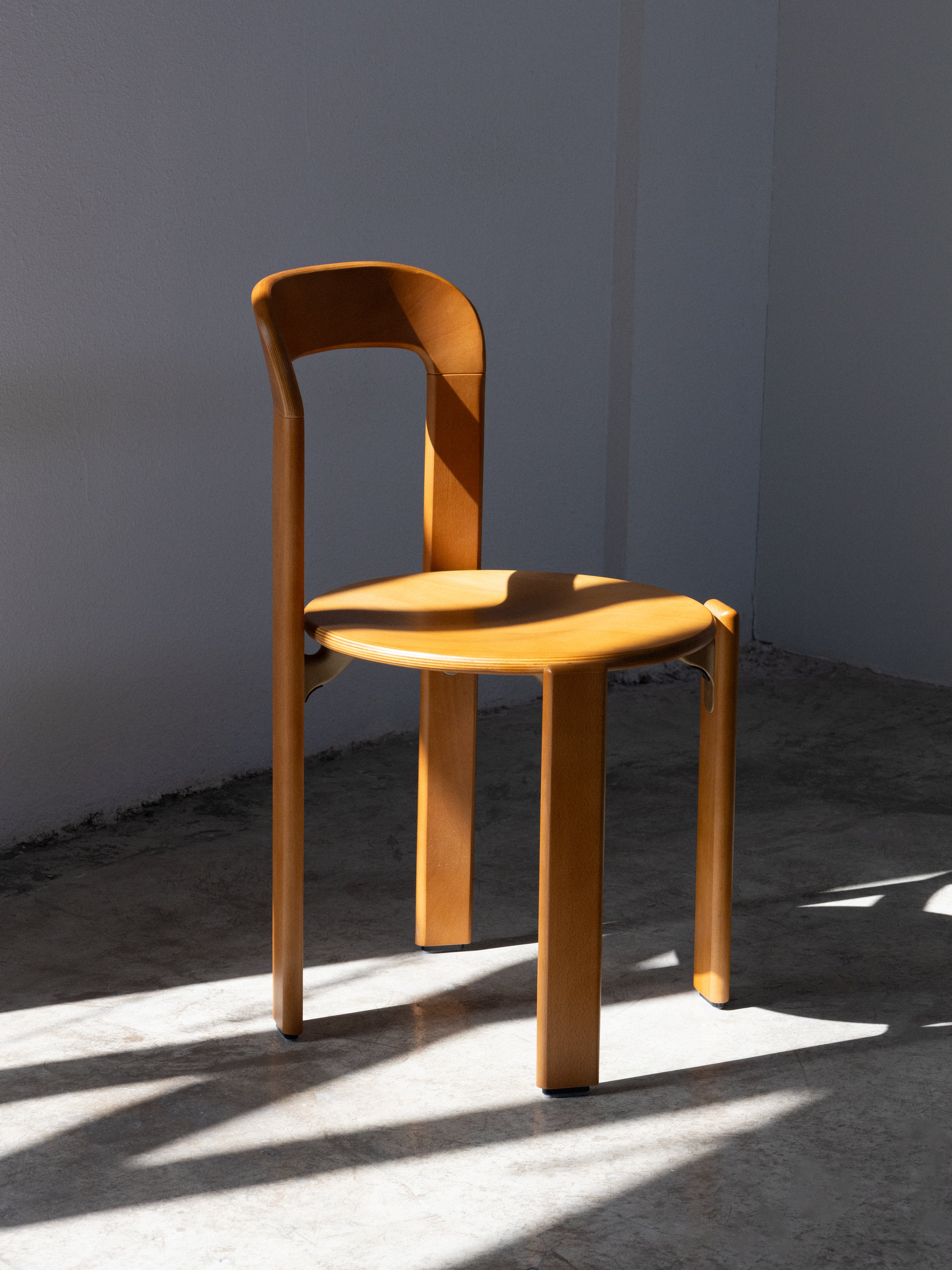 A wooden chair with a full backrest standing in a sunlit room.