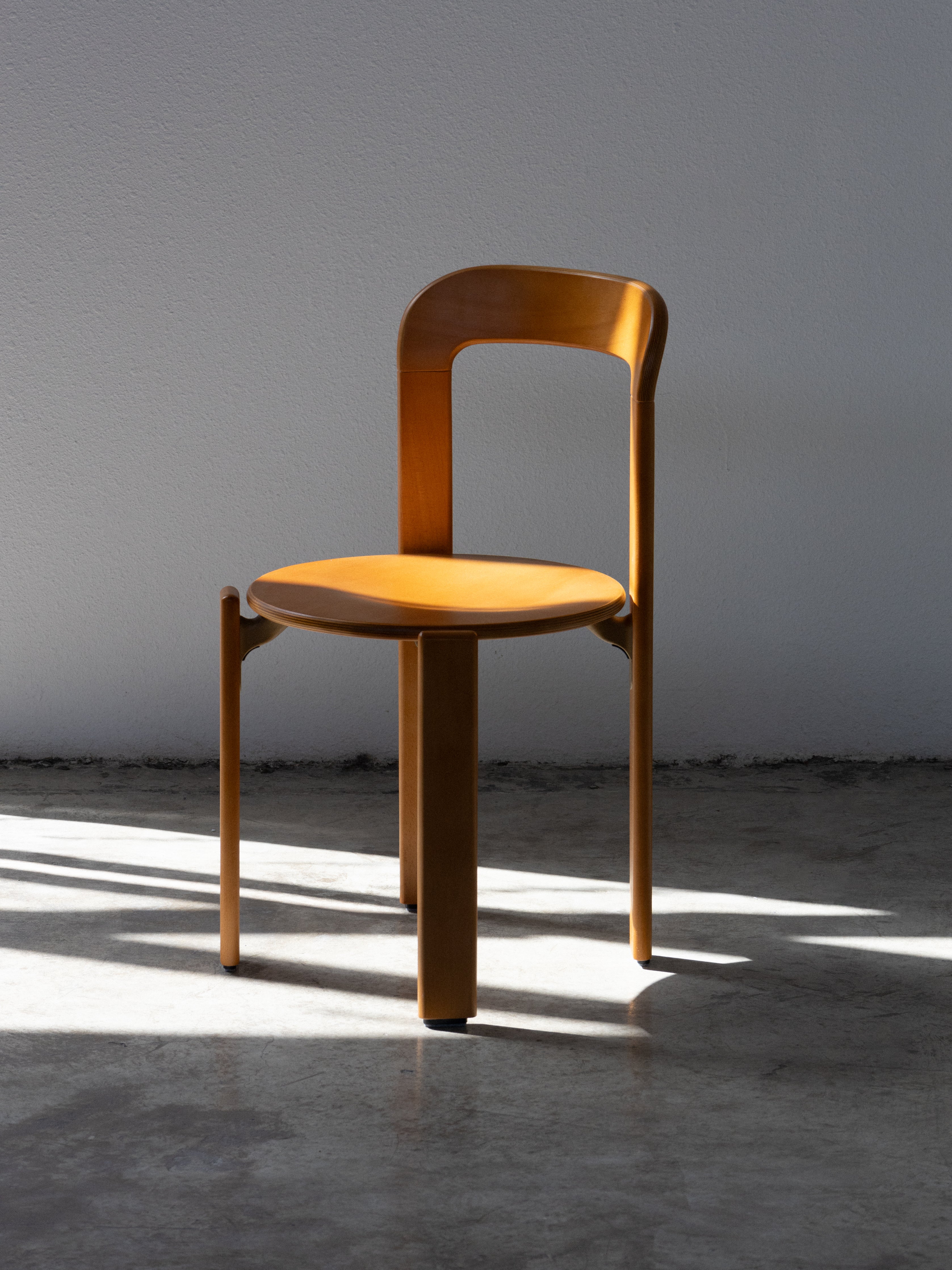 Wooden chair in a sunlit room with a concrete floor and gray wall. Rey Chair