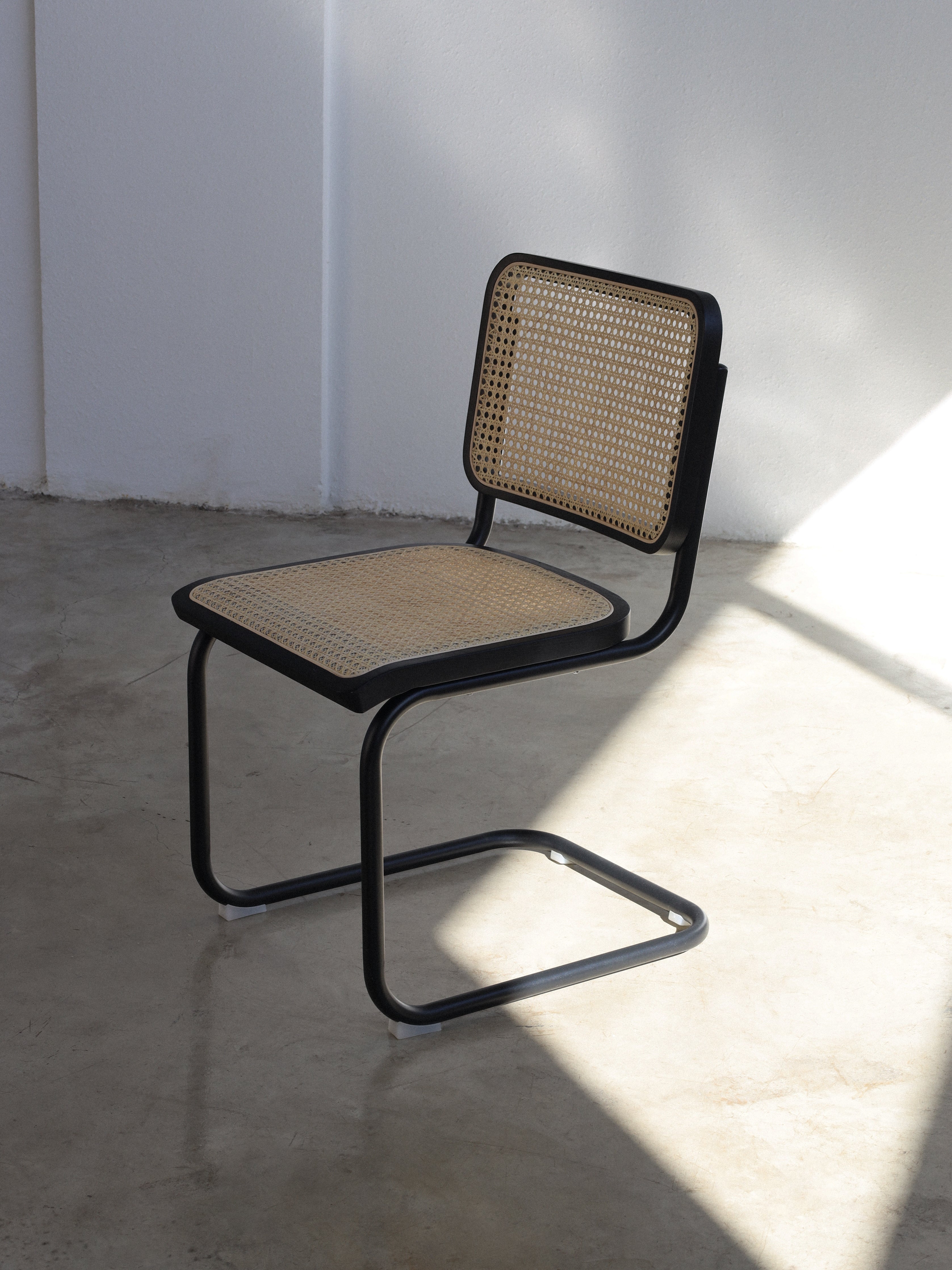 A Cesca chair with a black metal frame and a beige rattan seat and backrest, standing in a well-lit interior space.