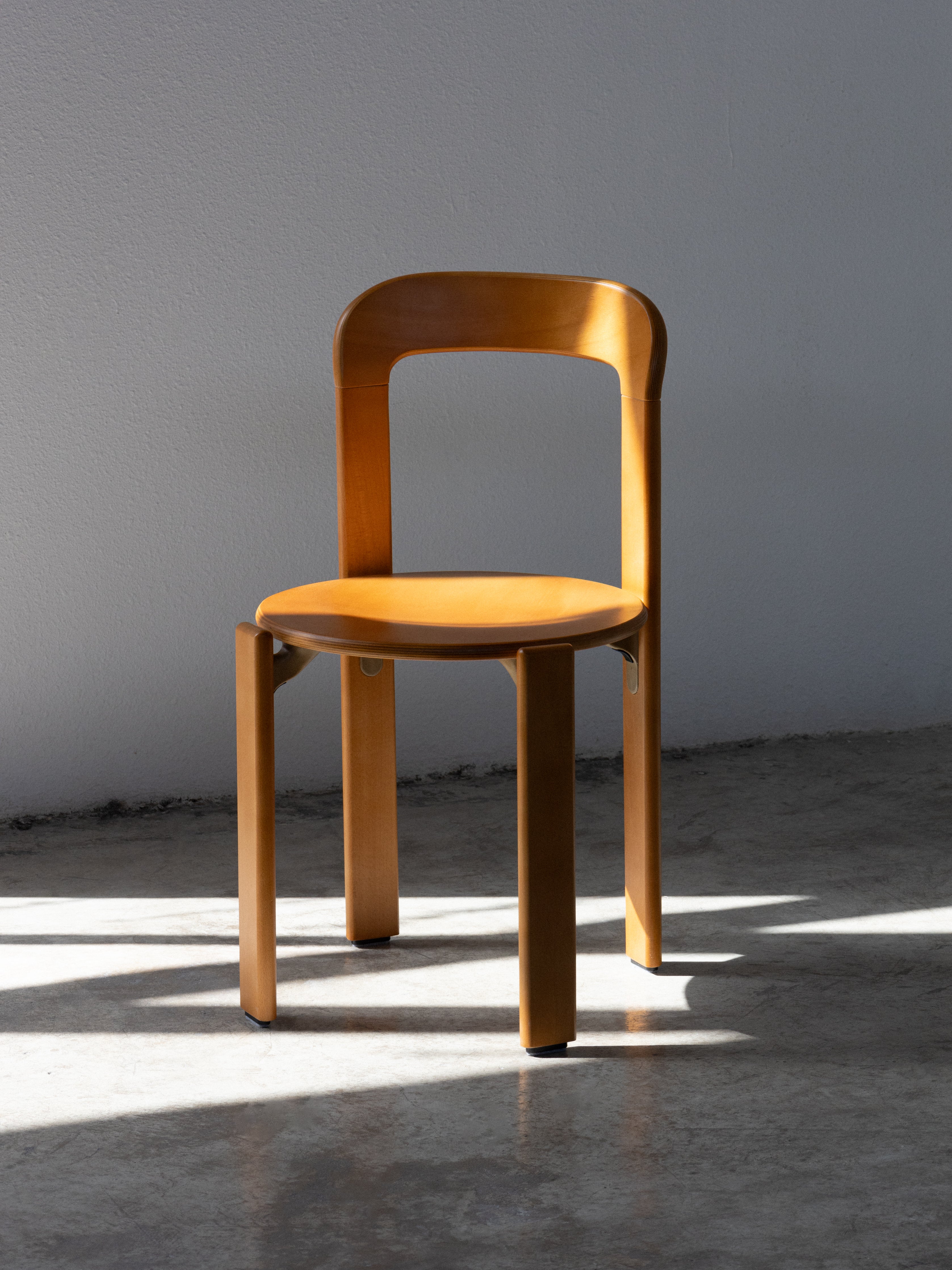 Wooden chair with orange seat cushion in a sunlit room. Rey Chair