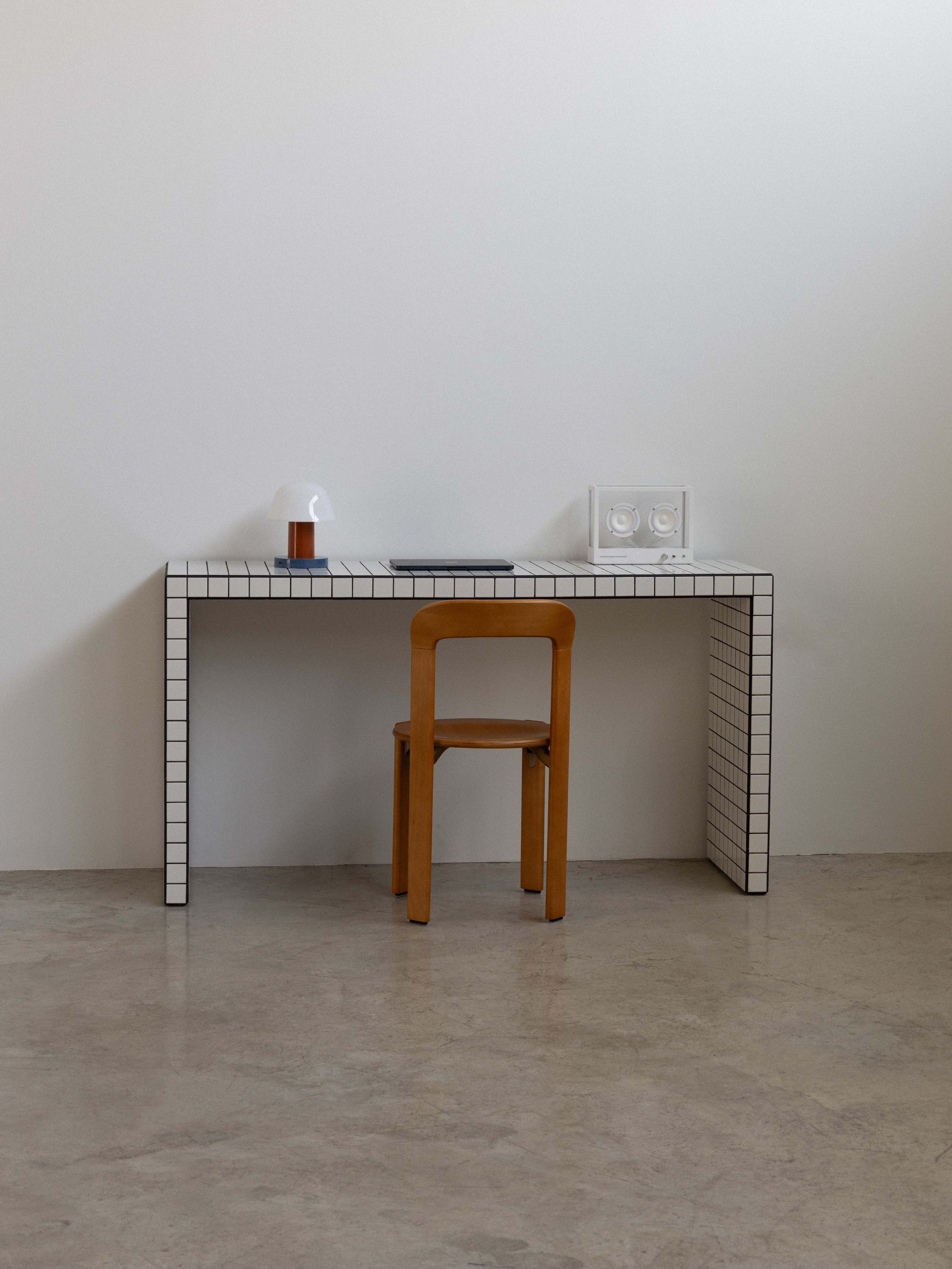 Minimalist desk with tiled surface and wooden chair against a plain wall.