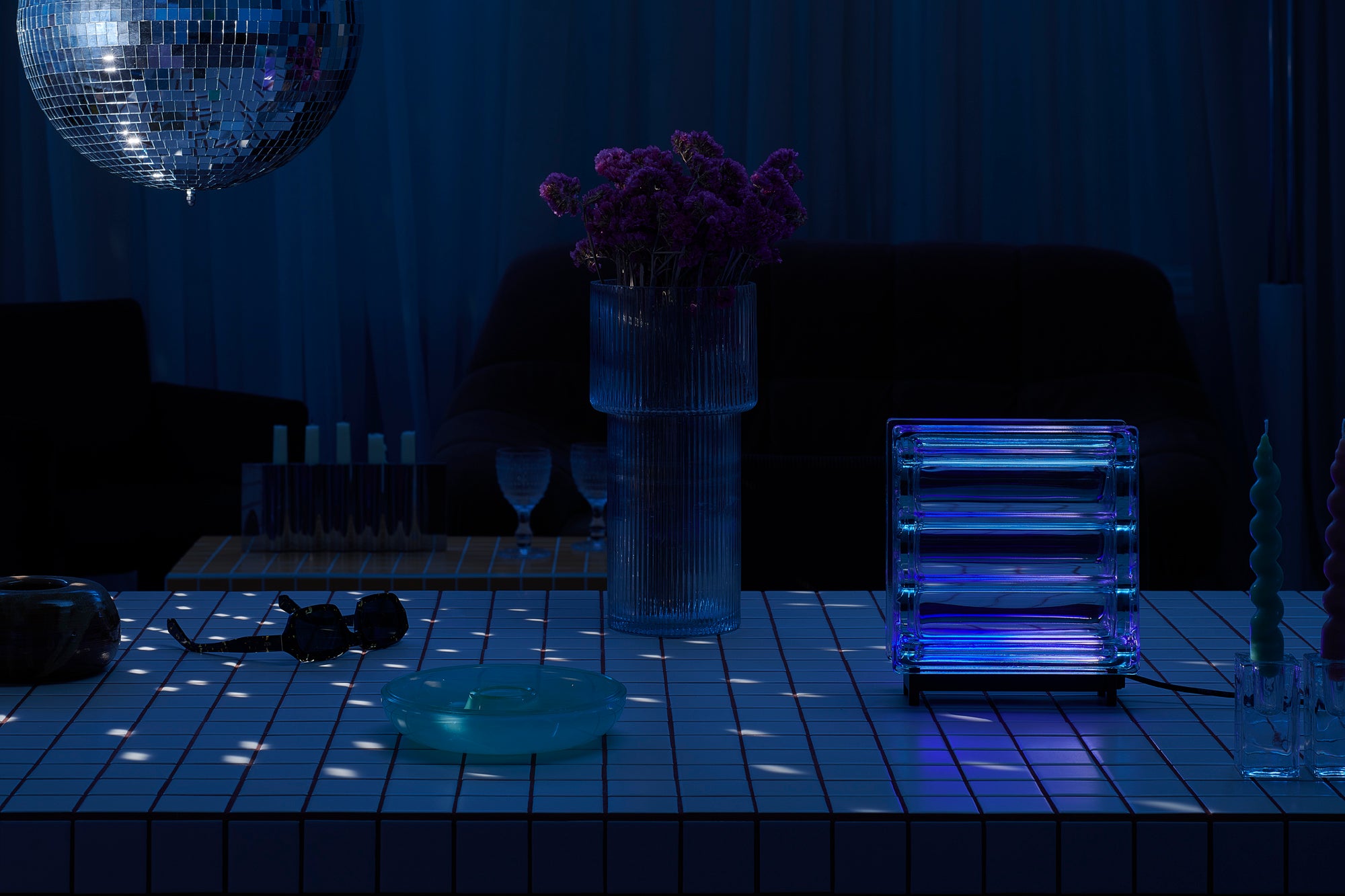 Dark room with disco ball, vase of flowers, and glass table.