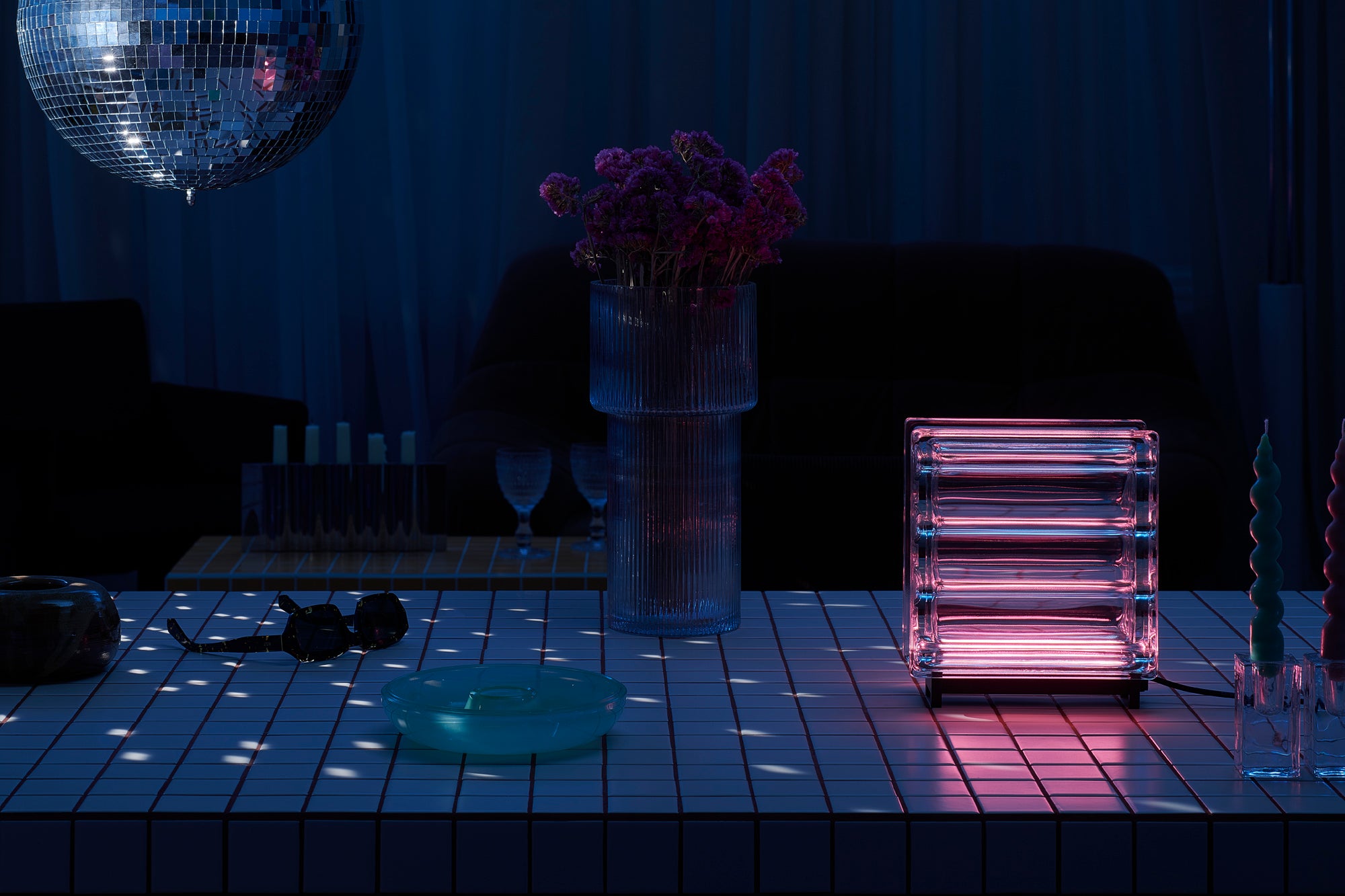 Modern interior with a vase of flowers, disco ball, and pink light fixture on a wooden table.