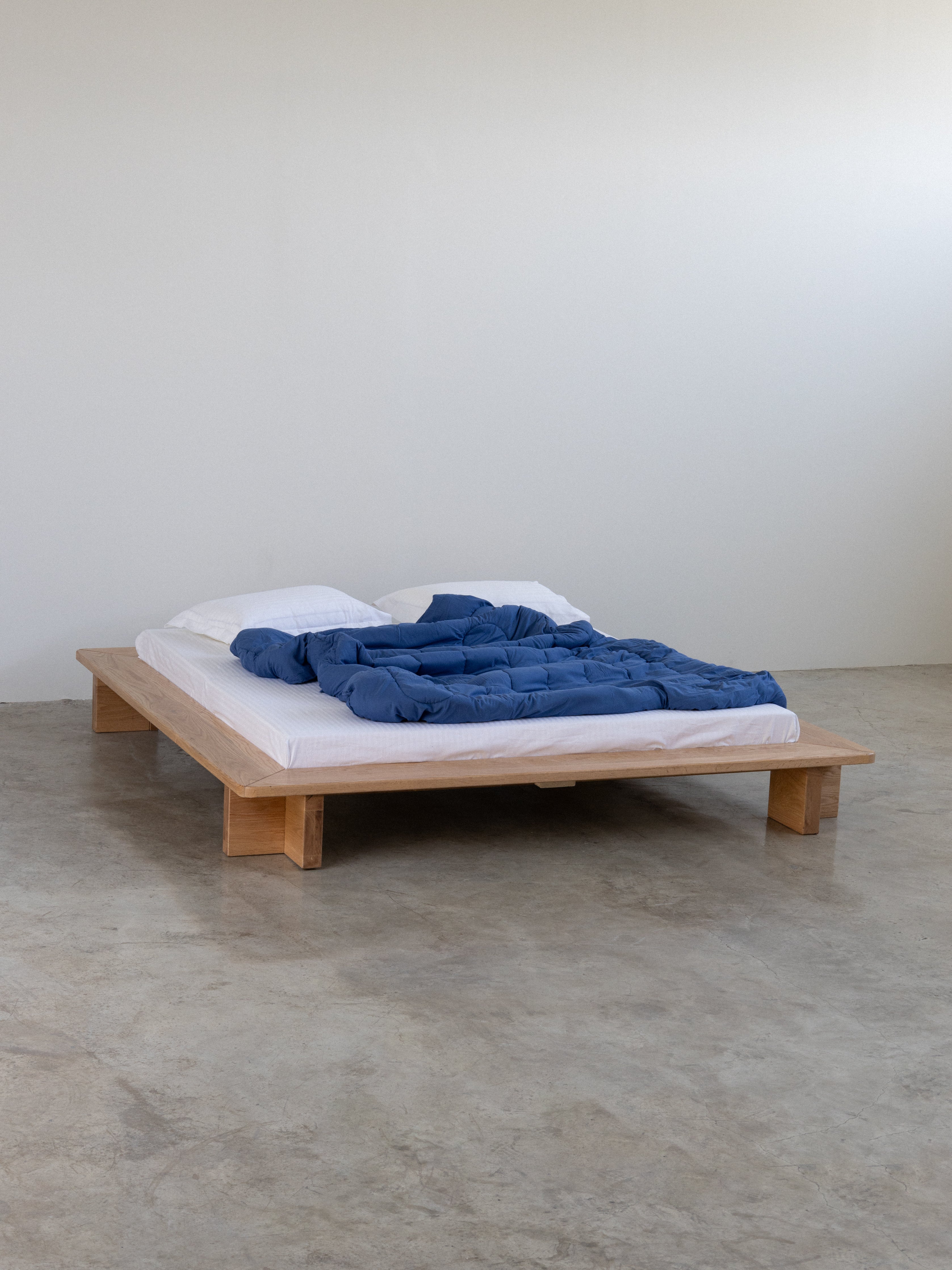 Wooden bed with a blue blanket on a concrete floor and white wall background