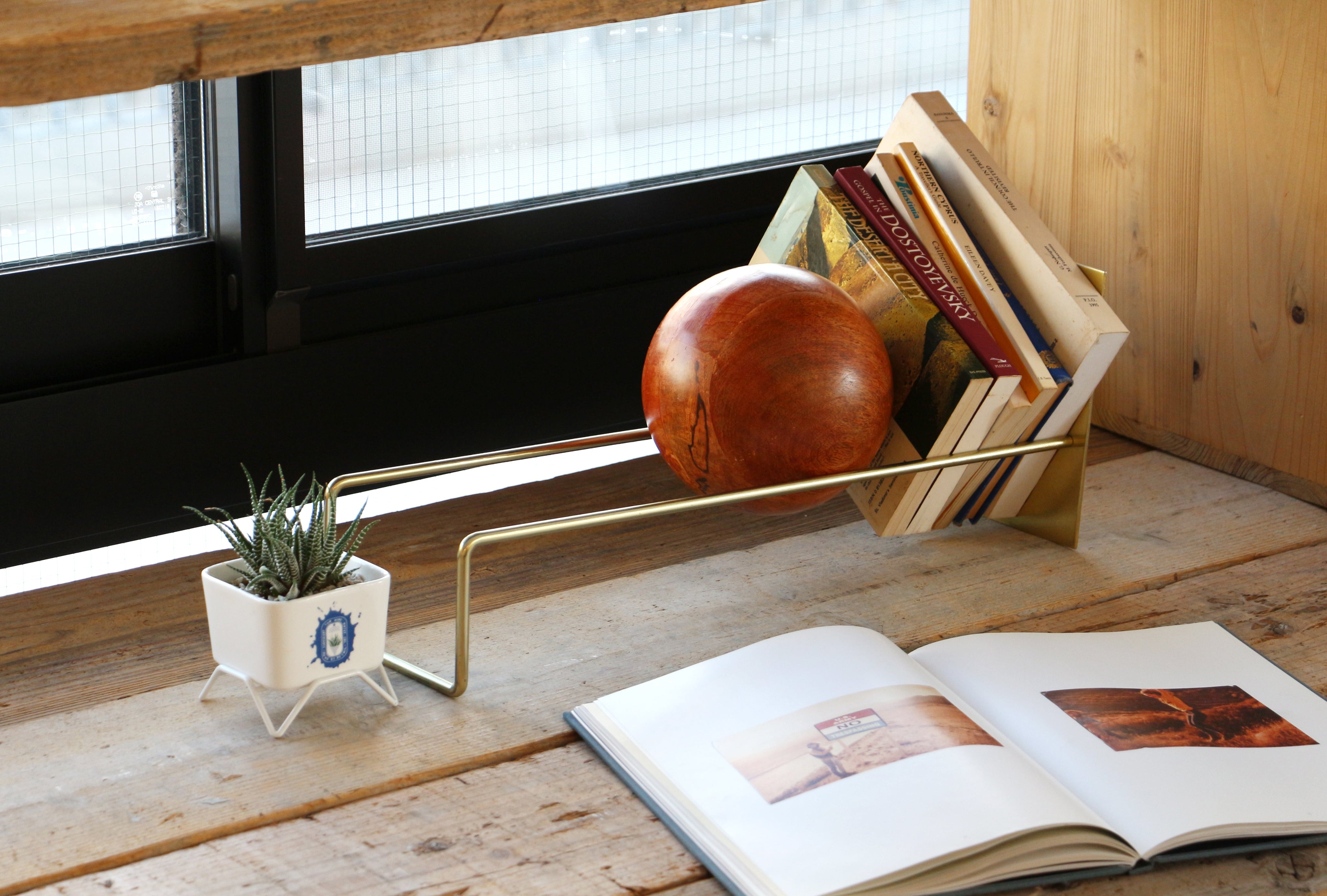 Gold bookend holding books on a wooden surface with an open book and small plant nearby.