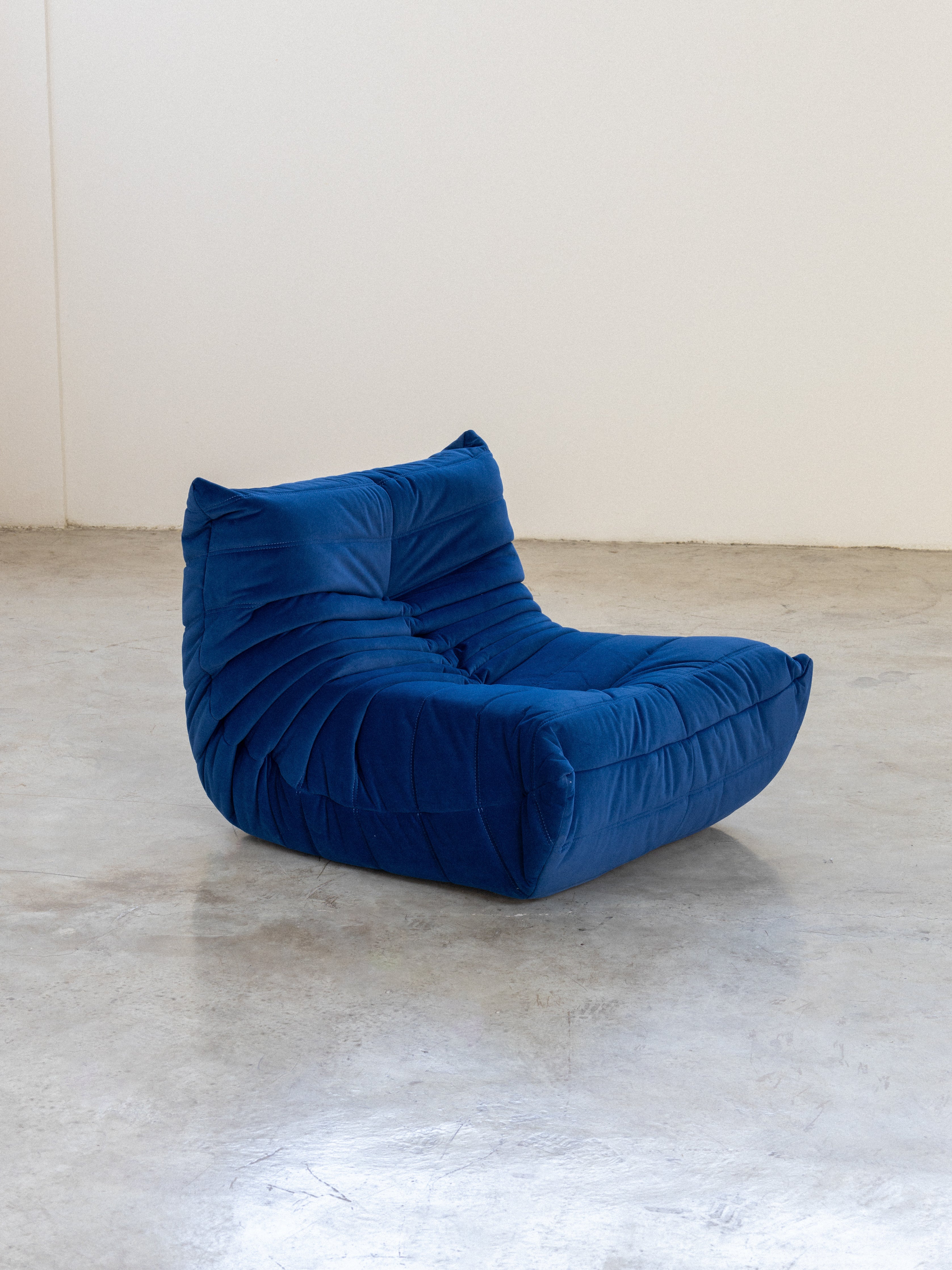 A blue velvet fabric Togo sofa on a plain background.