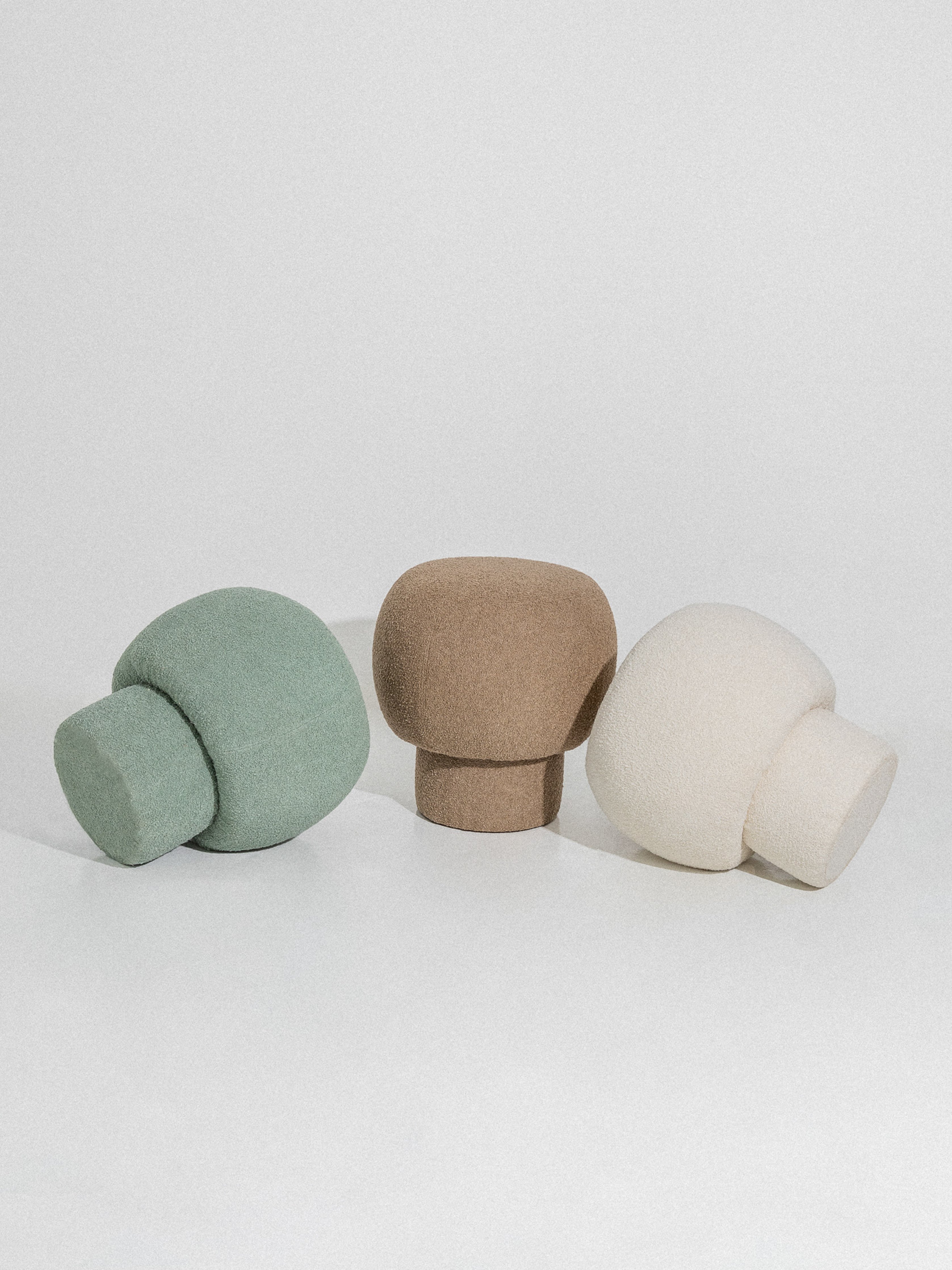 Three mushroom-shaped ottomans in beige, green, and white, presented on a white background.
