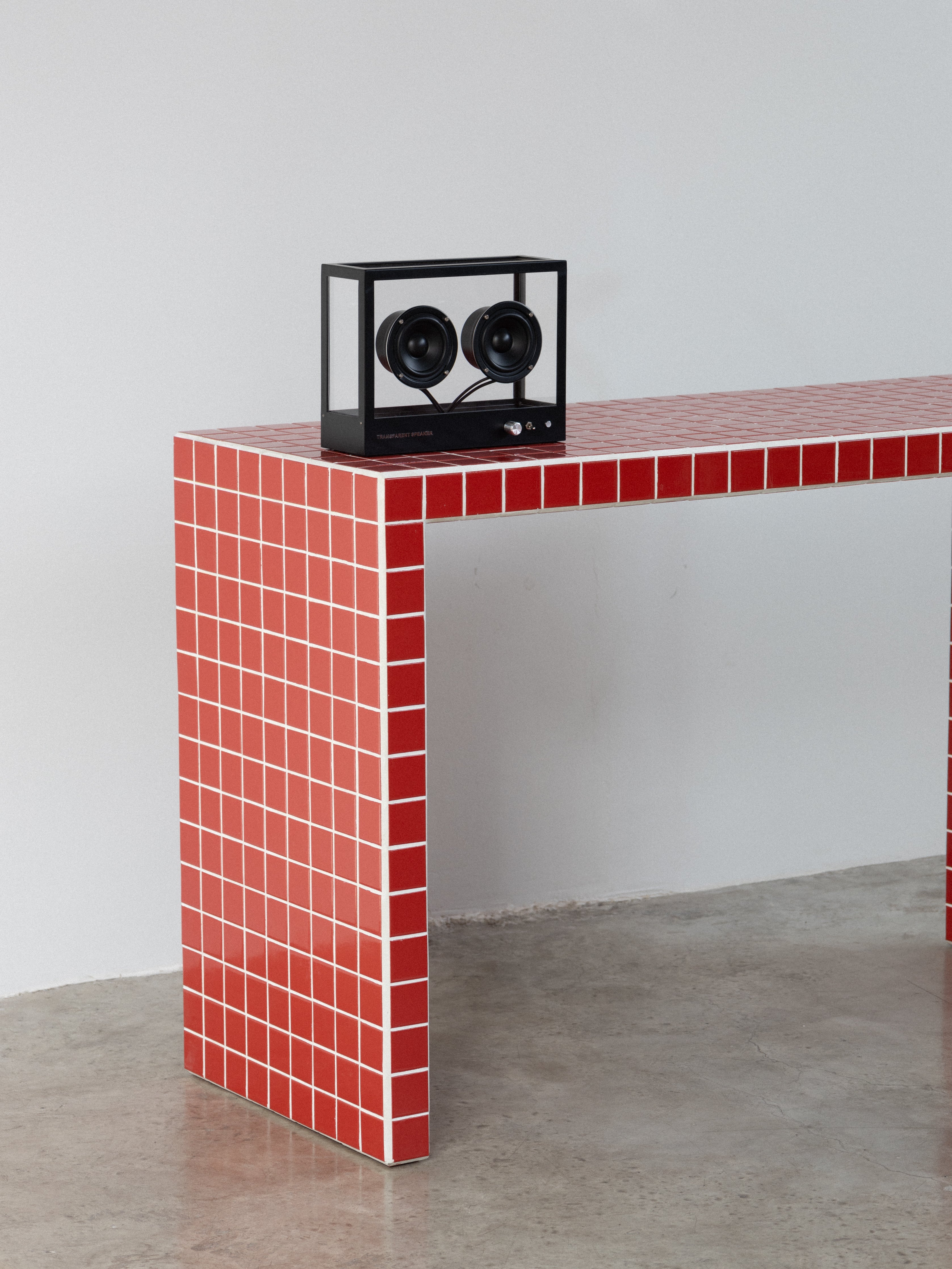 Red tiled console table with a black clock on a gray floor and wall.